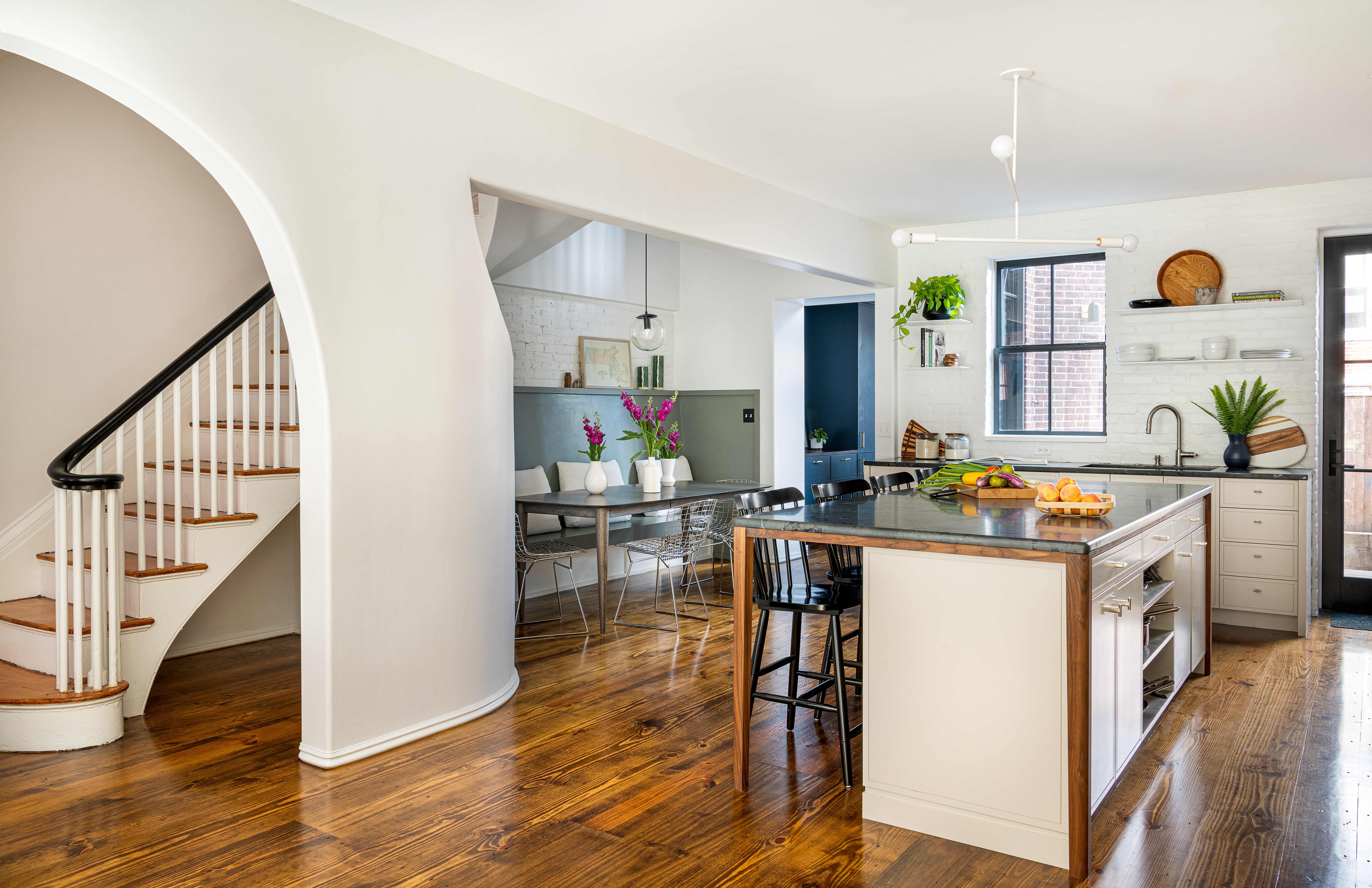 An Andrew Neyer chandelier hangs over the island, which has a walnut skirt frame and legs. The banquette is painted Benjamin Moore’s Cos Cob Stonewall. A Cedar & Moss pendant hangs from the second-story ceiling over an extension table from Circle Furniture.