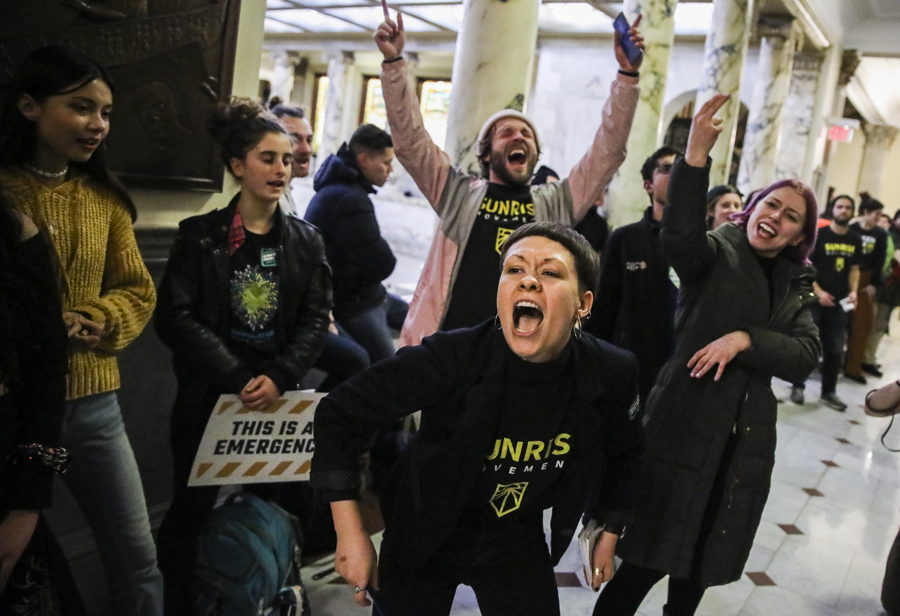 Sunrise Movement organizer Sarah Duckett lead a chant with about 100 other activists as they assembled in front of Governor Charlie Baker’s office at the State House on Dec. 6.