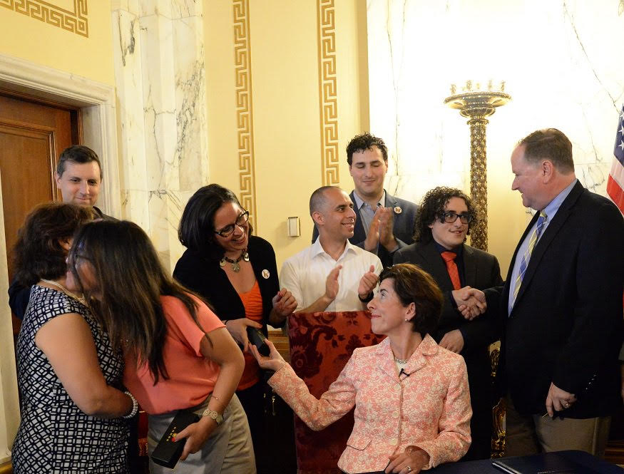 Rodrigo Pimentel, second from right, shakes hands with Senate Majority Leader Michael J. McCaffrey after Governor Gina M. Raimondo, seated, signed a 2018 bill ensuring driver's licenses are available to those in the Deferred Action for Childhood Arrivals (DACA) program.