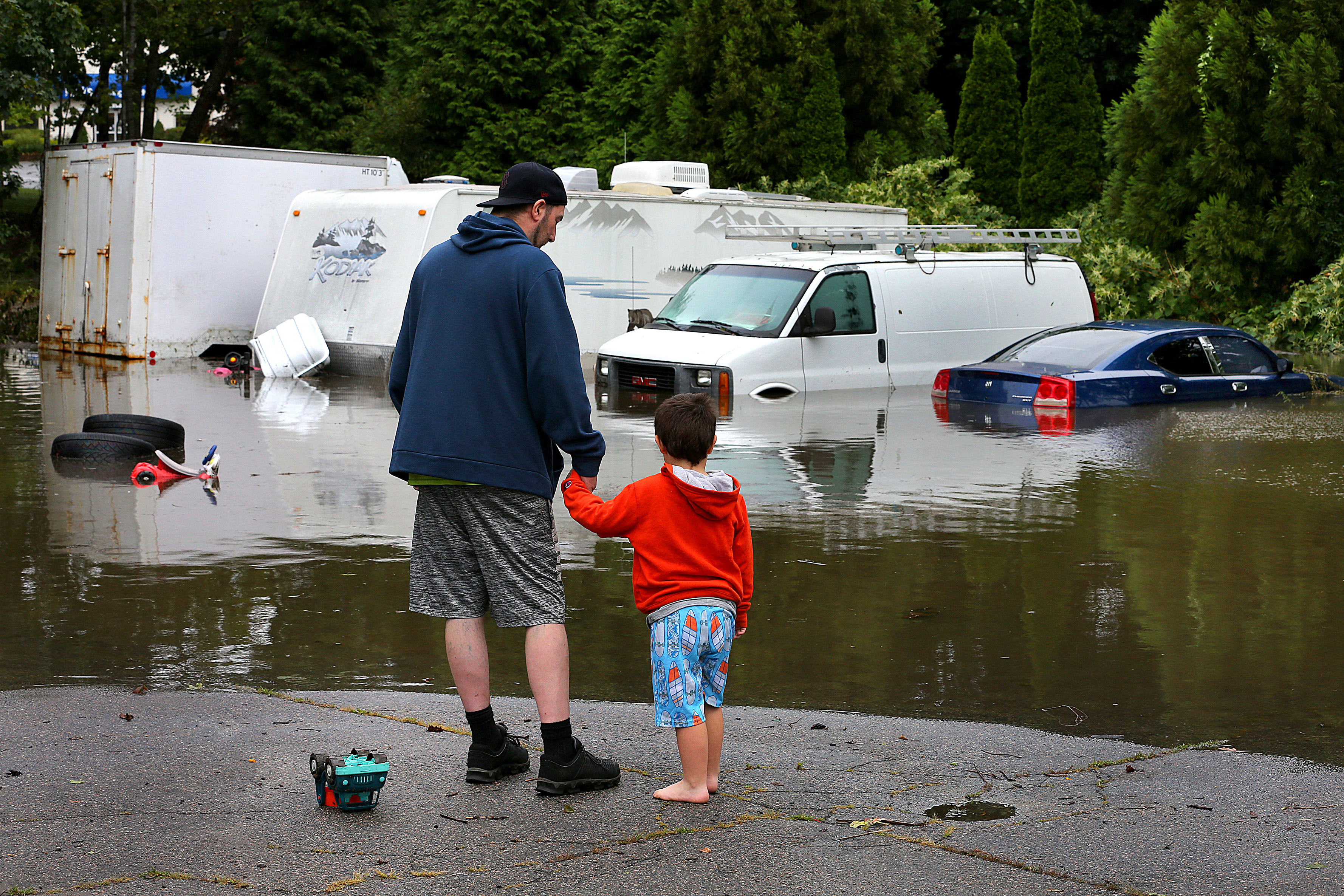 Ed Kelley and his son, Austin, 4, surveyed his car and his neighbor’s camper and van in the the flooded parking lot behind his apartment on Main Street in Kingston on Thursday.