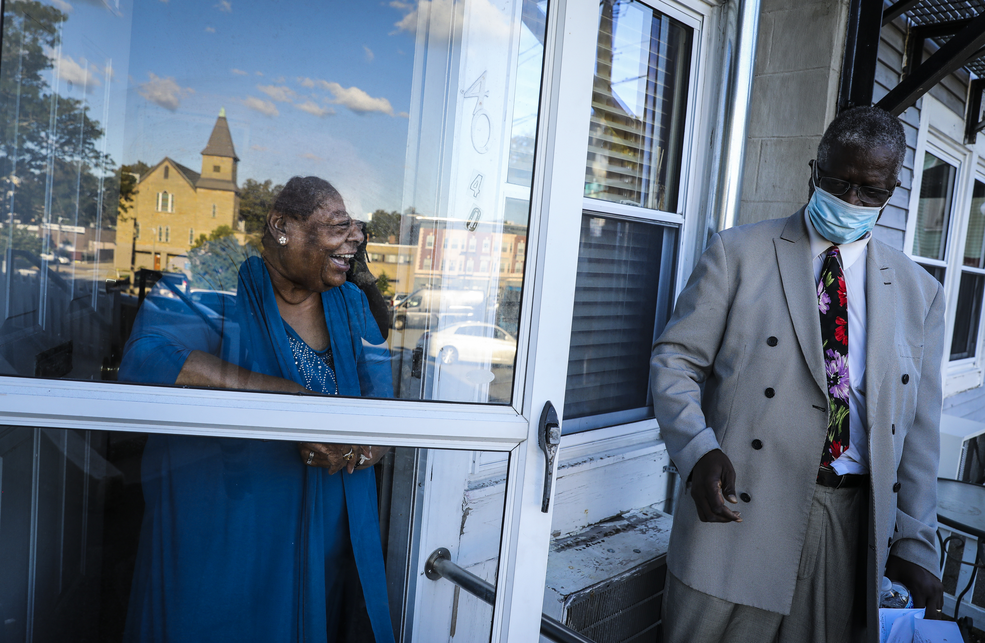 Twelfth Baptist Church is reflected in Roxbury resident Eva Coakley’s door while she chatted with the Rev. Vernard Coulter during a stop on the weekly peace walk with members of Twelfth Baptist Community Church and other local churches in Roxbury.