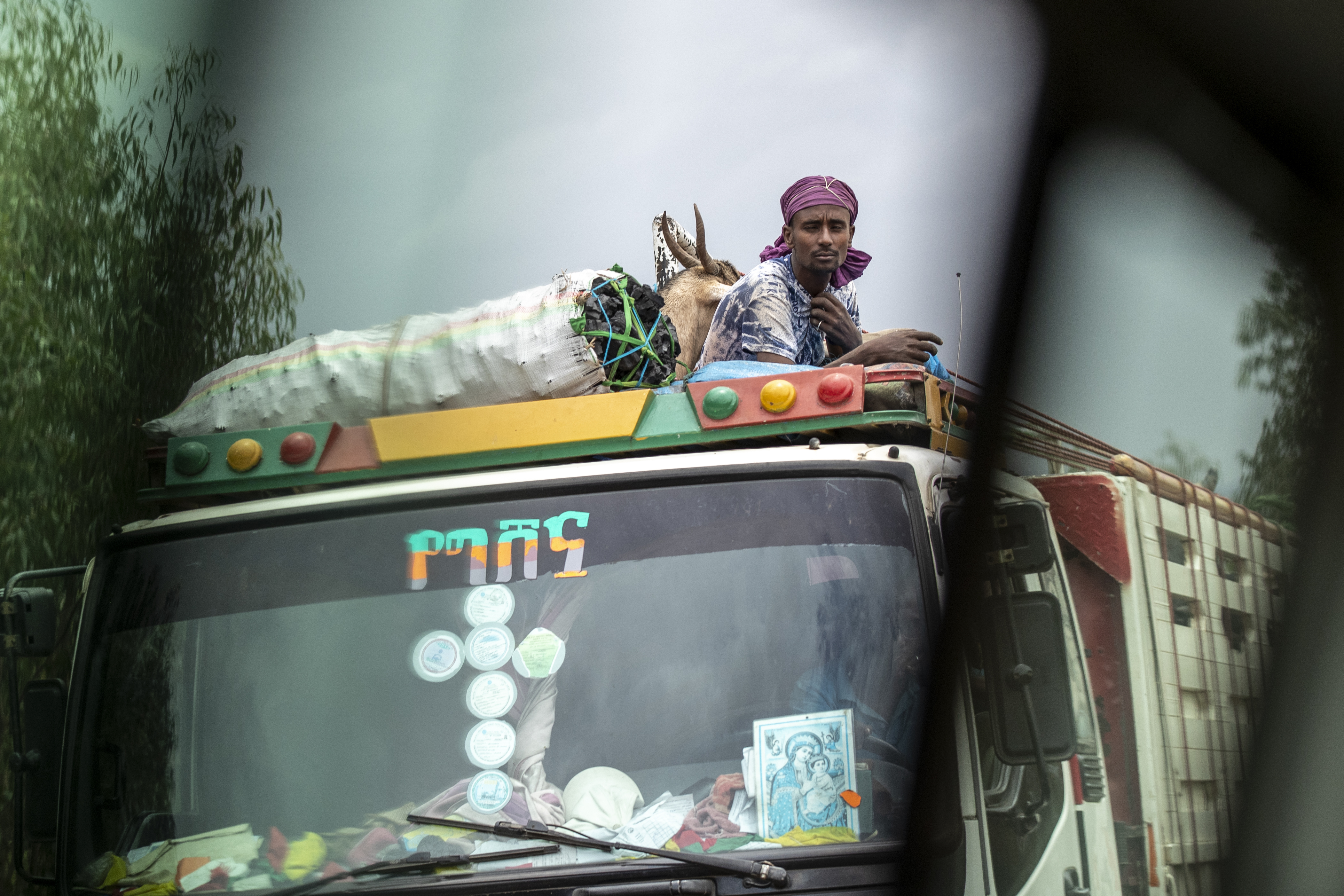 A man rides with goats and charcoal on the roof of a truck, seen through the window of a vehicle, in Ethiopia on May 1.