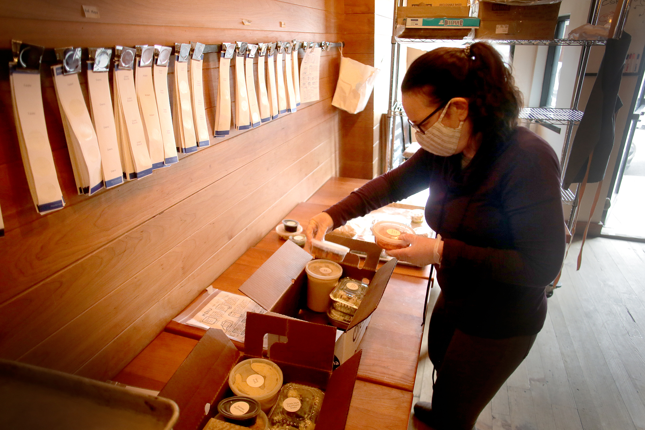 Restaurant Oleana in Cambridge provides complete subscription meals in a box similar to a farm share. Jenna Lyons, director of marketing at Oleana and Sofra, packs a box for a customer who picks up from the restaurant's takeout window.