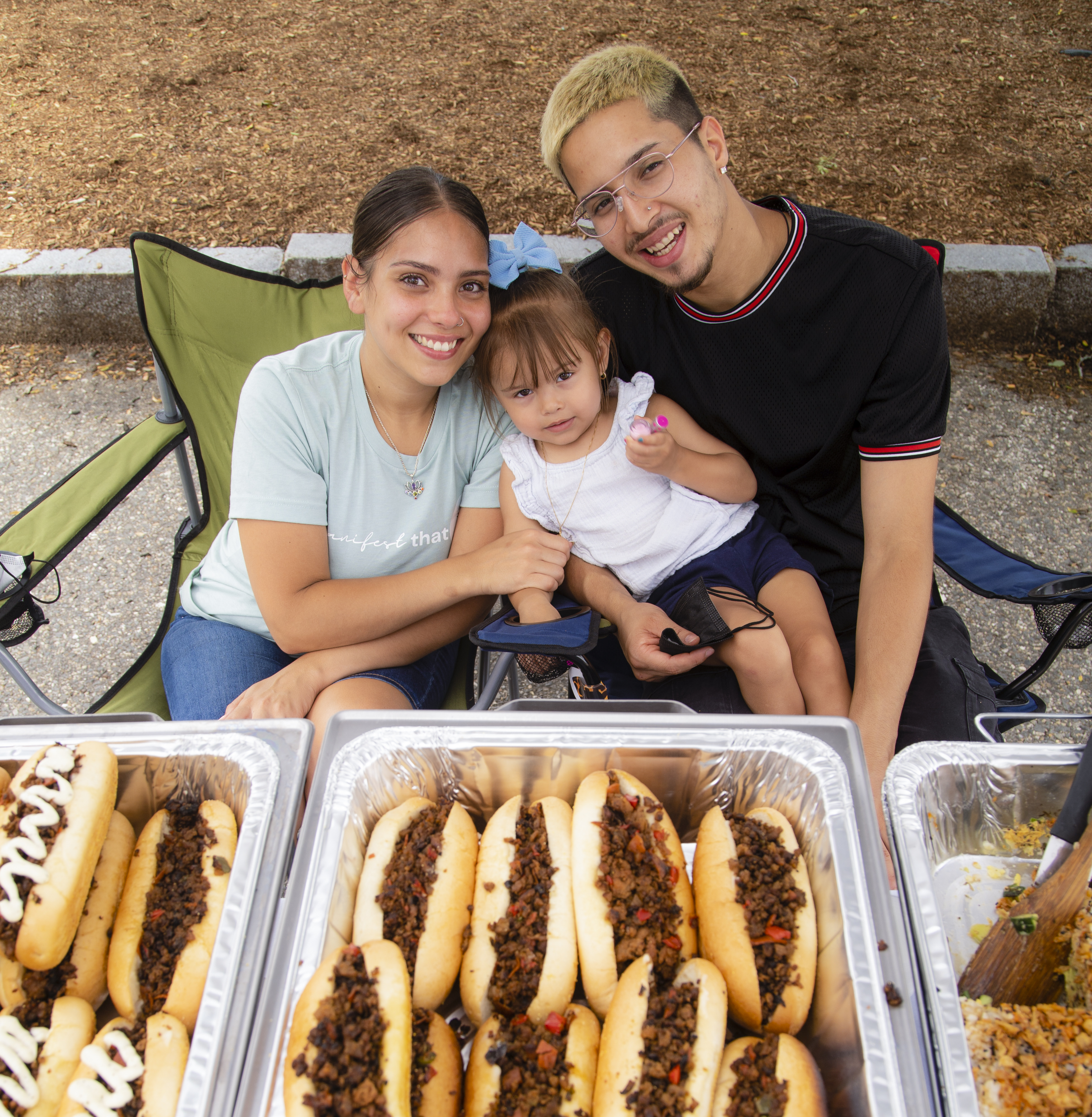 Viviana Torres of Viv's Garden, Sebastian Flores, and their daughter, Aleena, sit at their stall at a vegan market in Dover, NH, on Sunday.  Their offerings include the Whistle Bomb, a vegan take on a steak bomb.