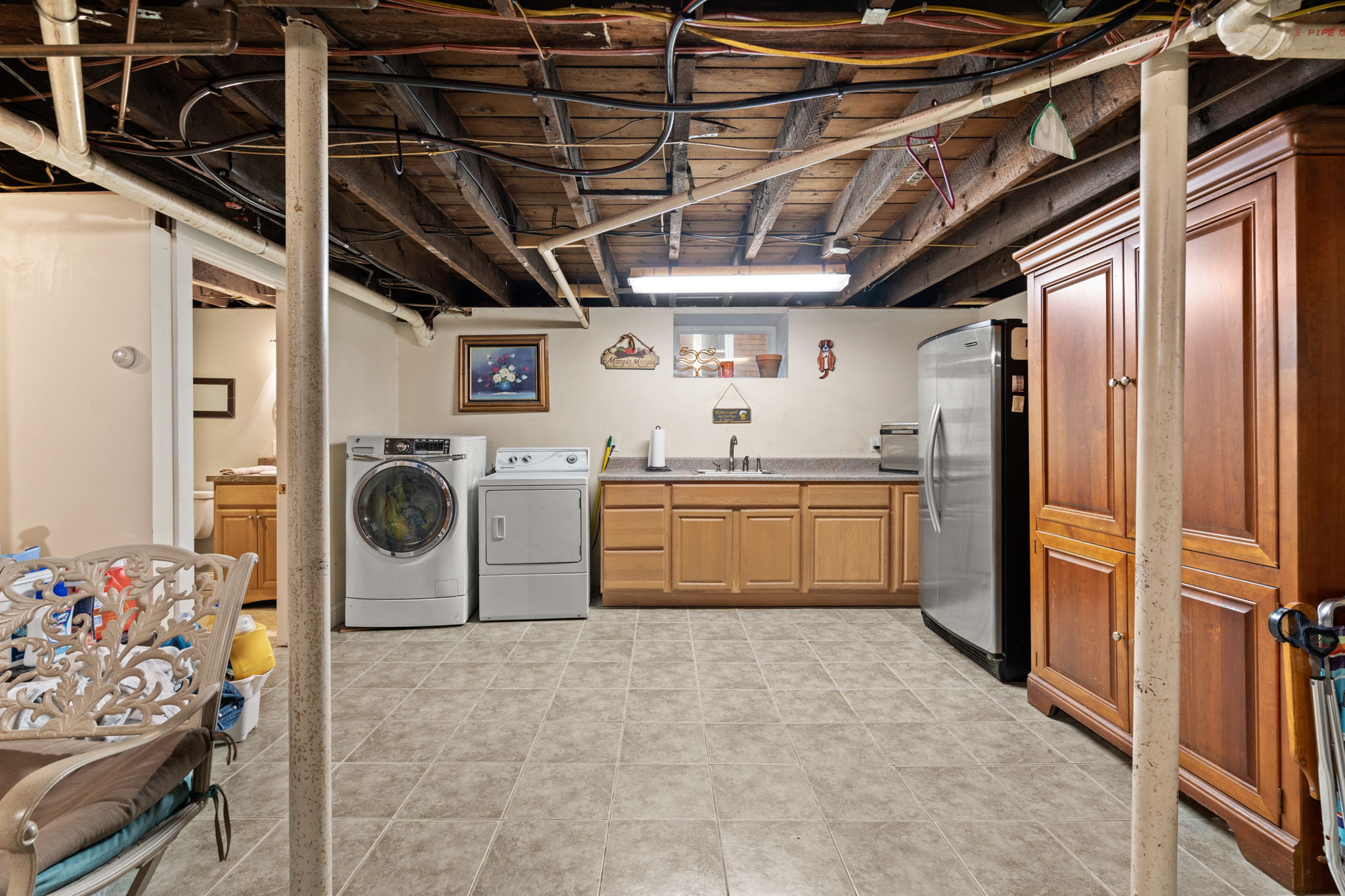 A view of the basement with tile floor, cabinetry, columns, exposed joists, and a laundry setup.