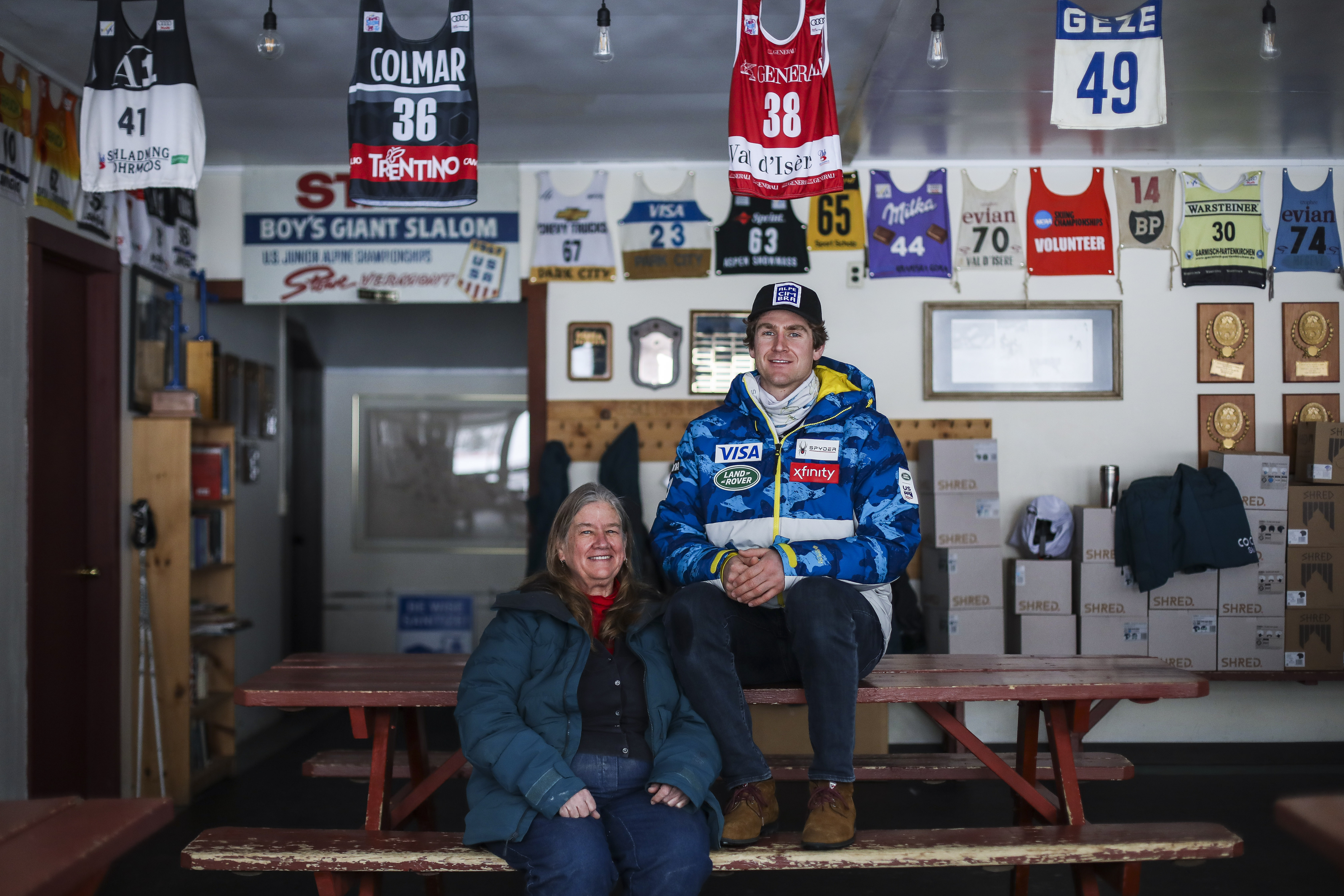 Ryan Cochran-Siegle and Barbara Ann Cochran at the family ski lodge in Richmond, Vt., where racing bibs worn by the family's many ski racers are displayed.