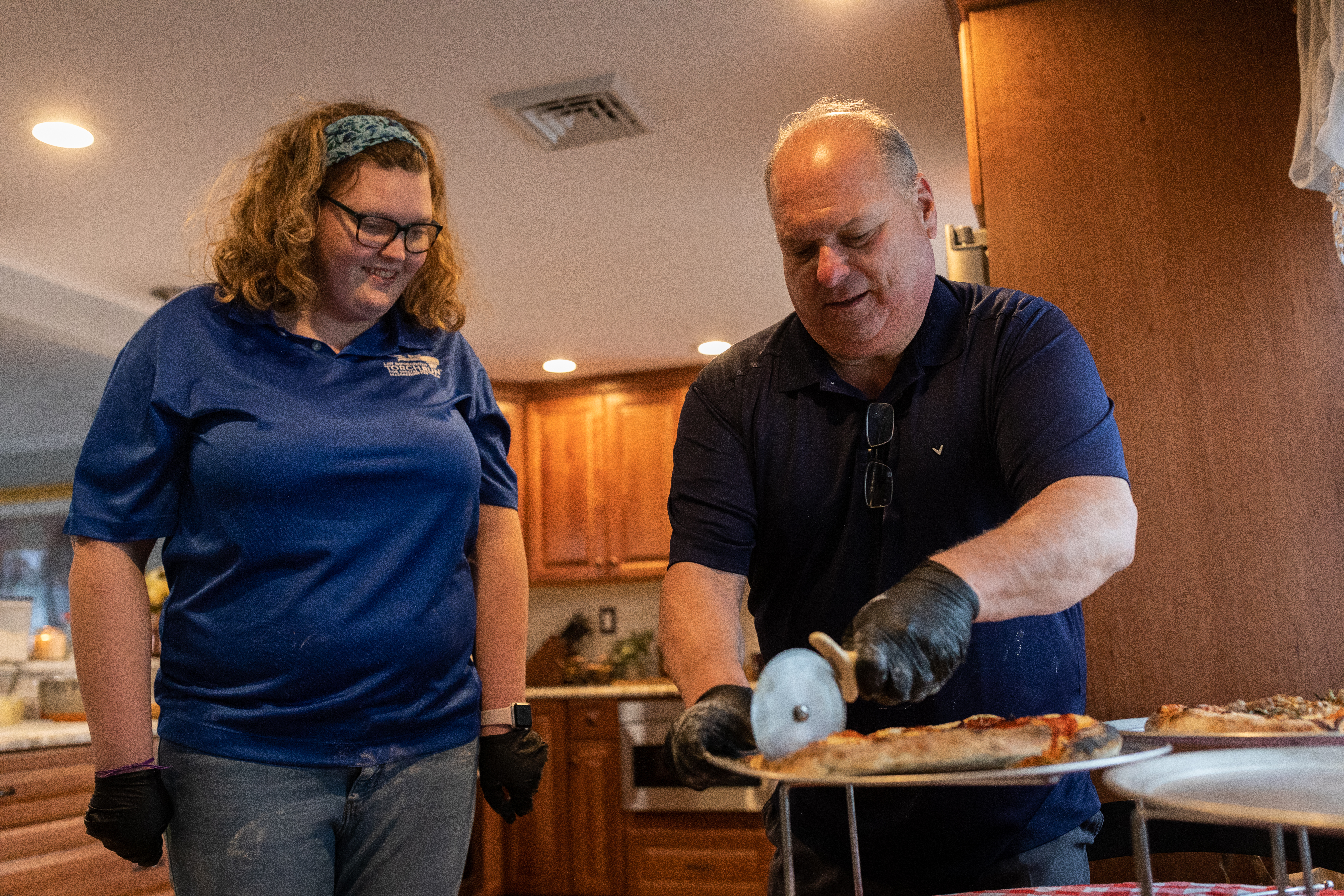 Meghan Colby, a Special Olympics athlete, watches as retired Middleton Police Chief Jim DiGianvittorio slices into a pizza during a live-streamed pizza cooking tutorial.