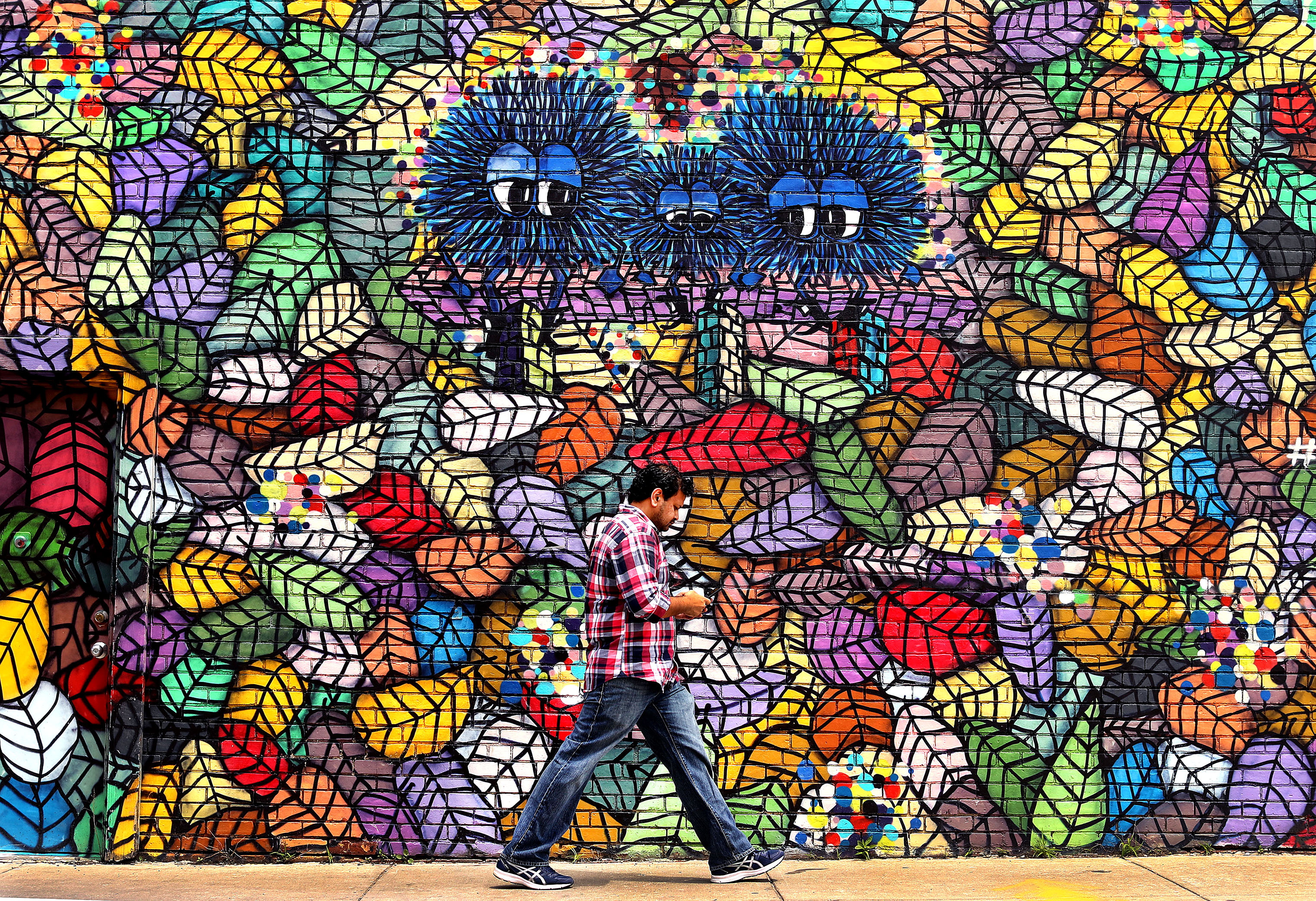 A man passed by a large mural on the side of a building on Denby Road in Allston. Called Fuzzy Creatures, it was painted by Boston artist Caleb Neelon.