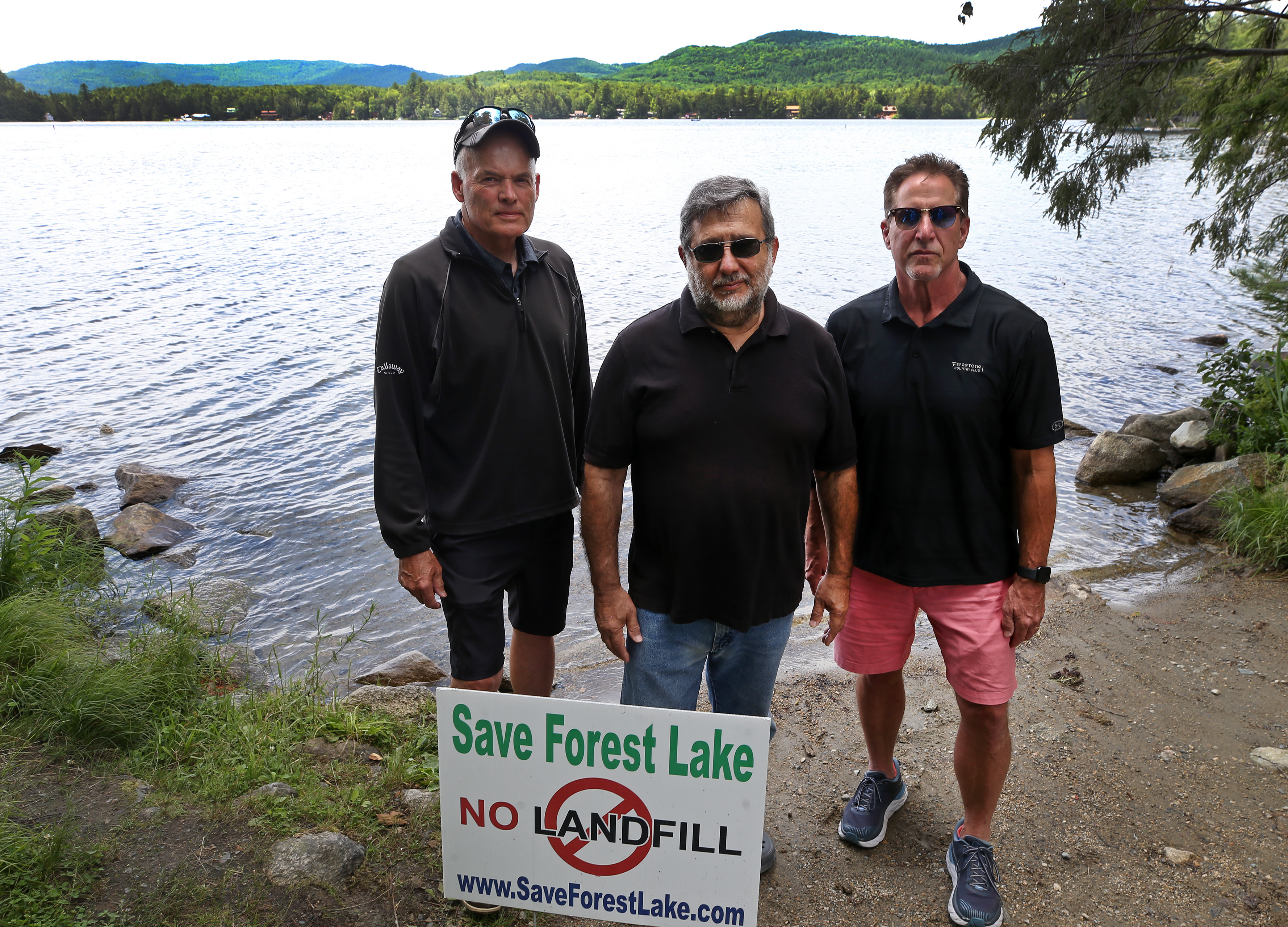 Pictured on the shore of Forest Lake are (left to right) Wayne Morrison, Eliot Wessler, and Tom Tower, with the proposed site of a landfill visible across the lake. It is proposed for the valley area seen behind Morrison.