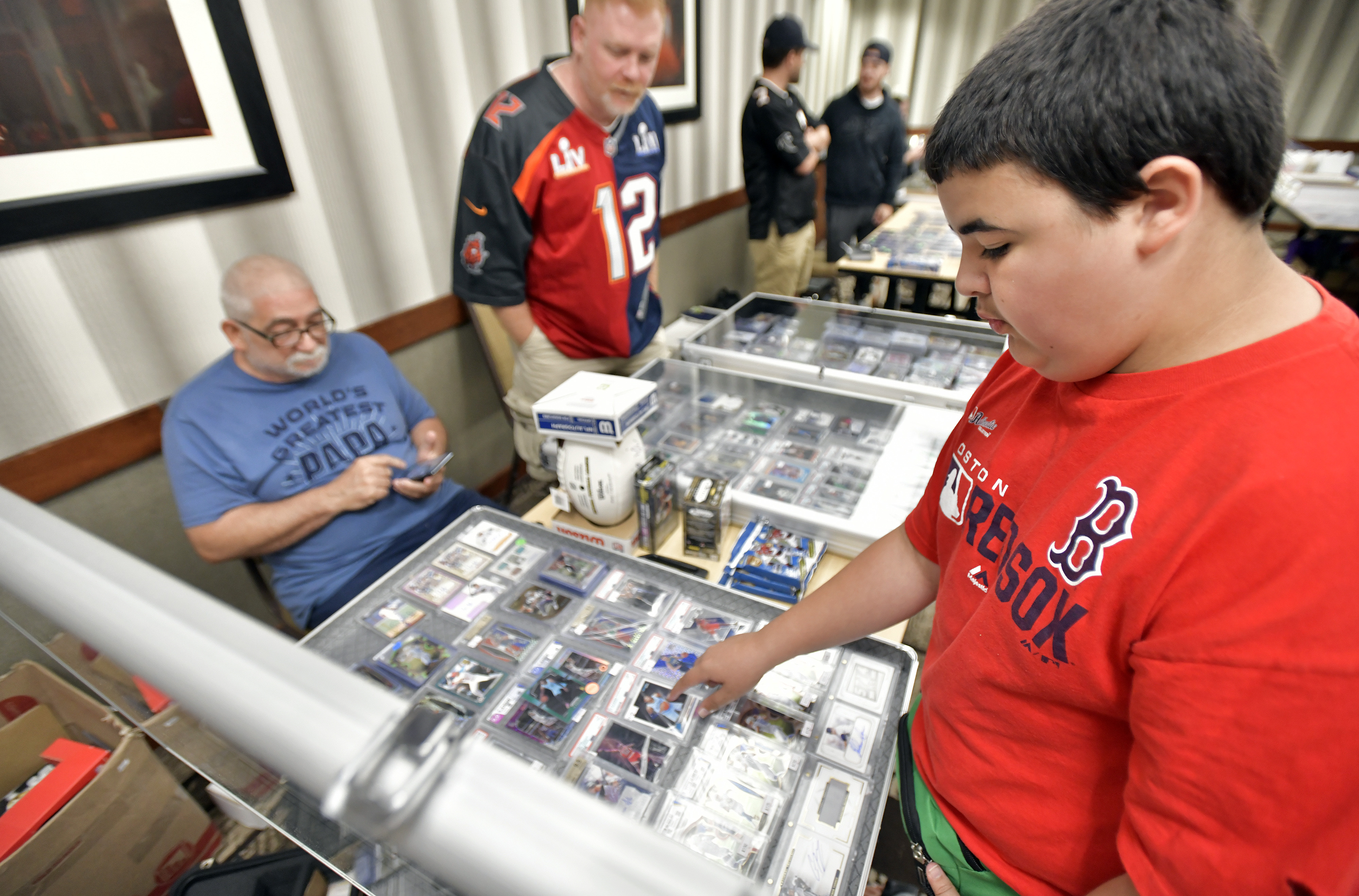 Davie Baia, 13, browses the table of father-and-son team WIlfred Bouchard of Fall River and Gregory Bouchard of Seekonk at the weekly Woburn Sportscard Show.