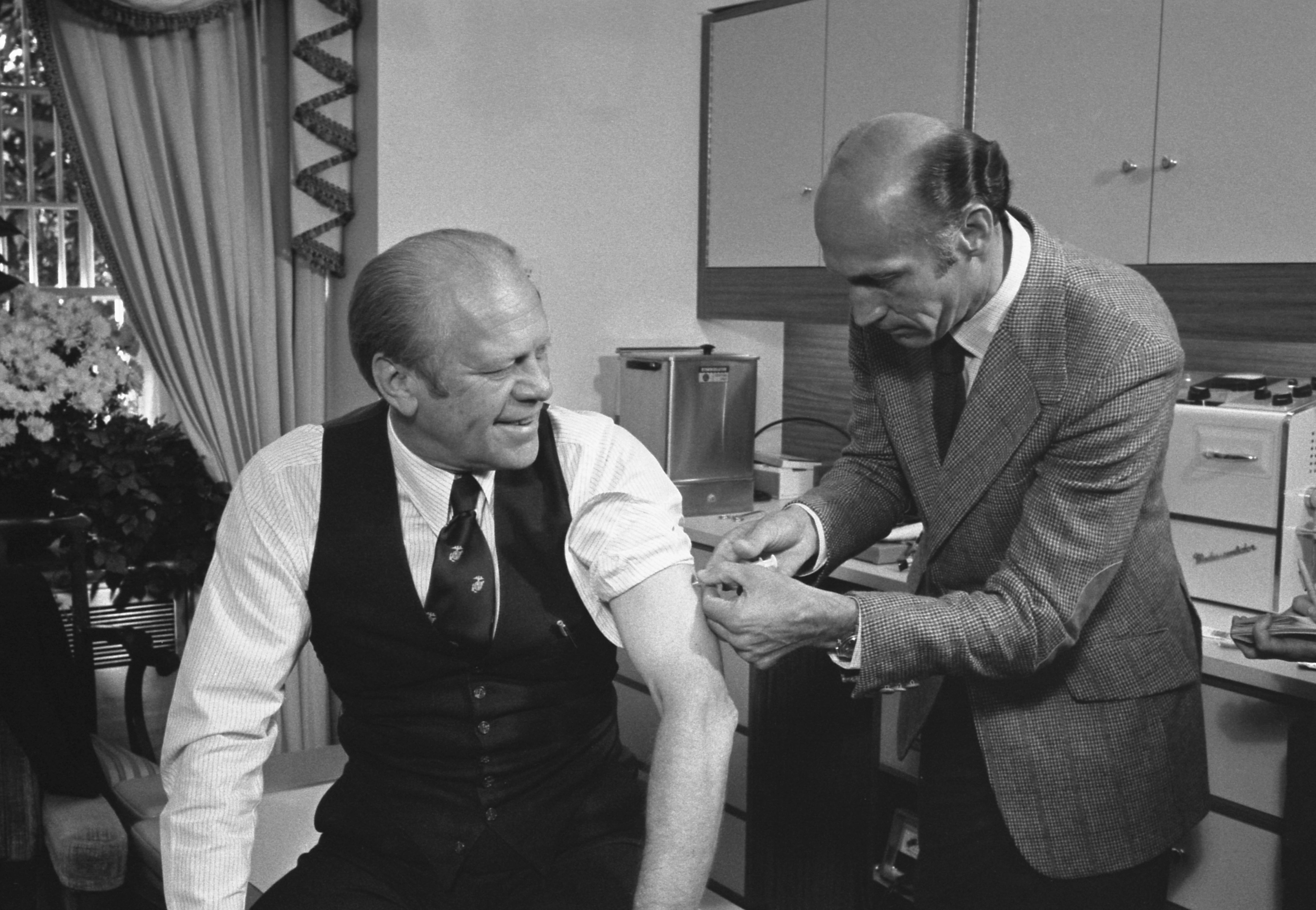 American politician US President Gerald Ford, his sleeve rolled up, was injected with a swine flu inoculation by White House physician Dr William Lukash, Washington DC, October 14, 1976.