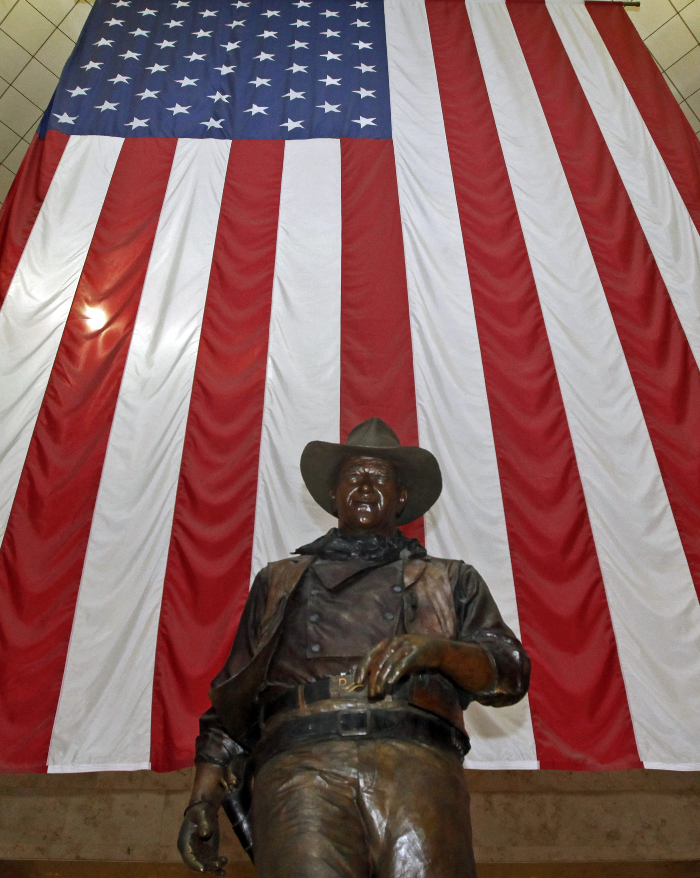 A bronze statue of late actor John Wayne stands before a four-story high United States flag at John Wayne Orange County Airport in Santa Ana, Calif.