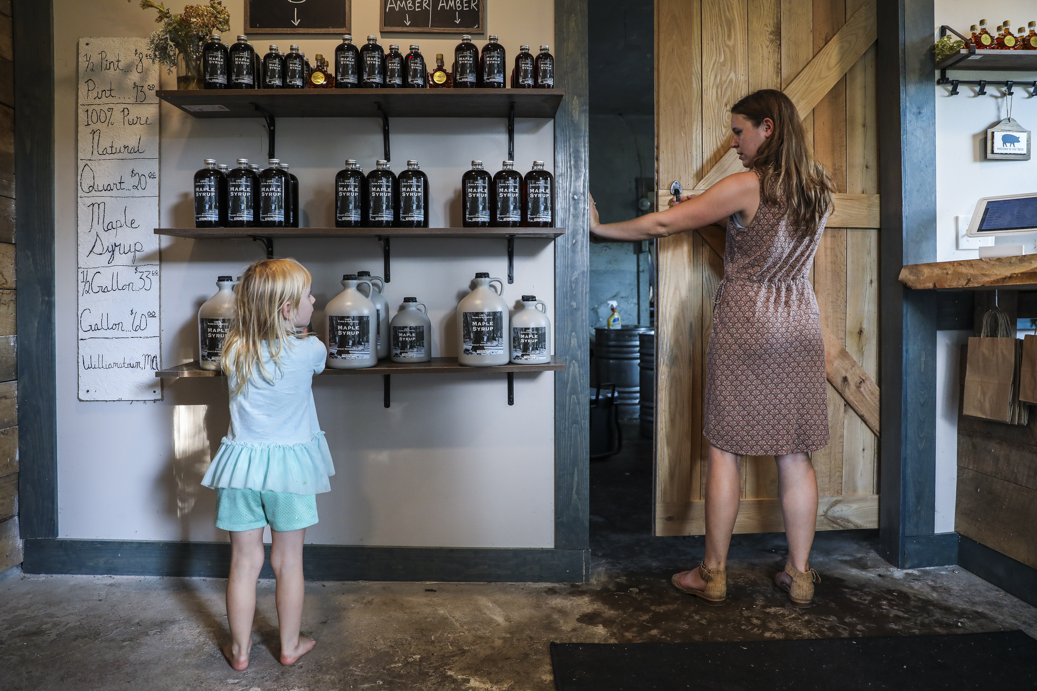 Nadia Lipinski, 5, moves around bottles of maple syrup in her family’s store while spending time with her mom, Sarah Lipinski, owner of Sweet Brook Farm.