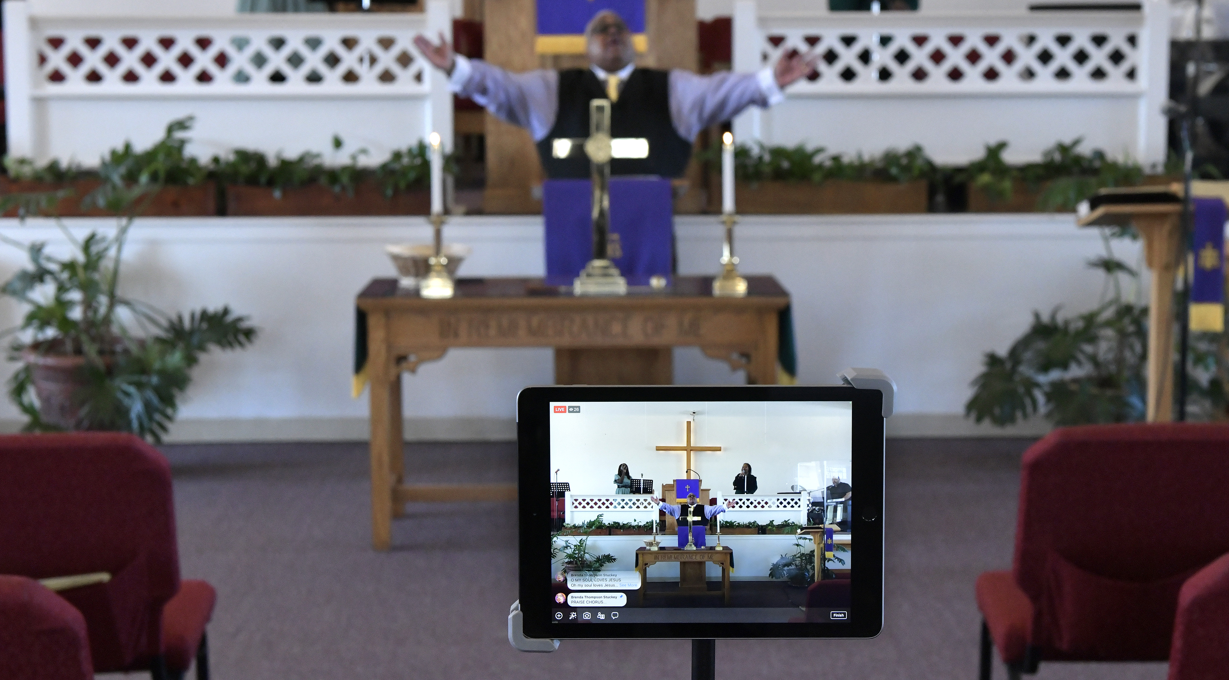 A tablet functions as a video monitor among empty pews during a remote service given by the Rev. Anthony Lloyd (center) with singers (from left) Marshalee Ellis-Kehlhem and Monica Anderson Spencer at The Greater Framingham Community Church.