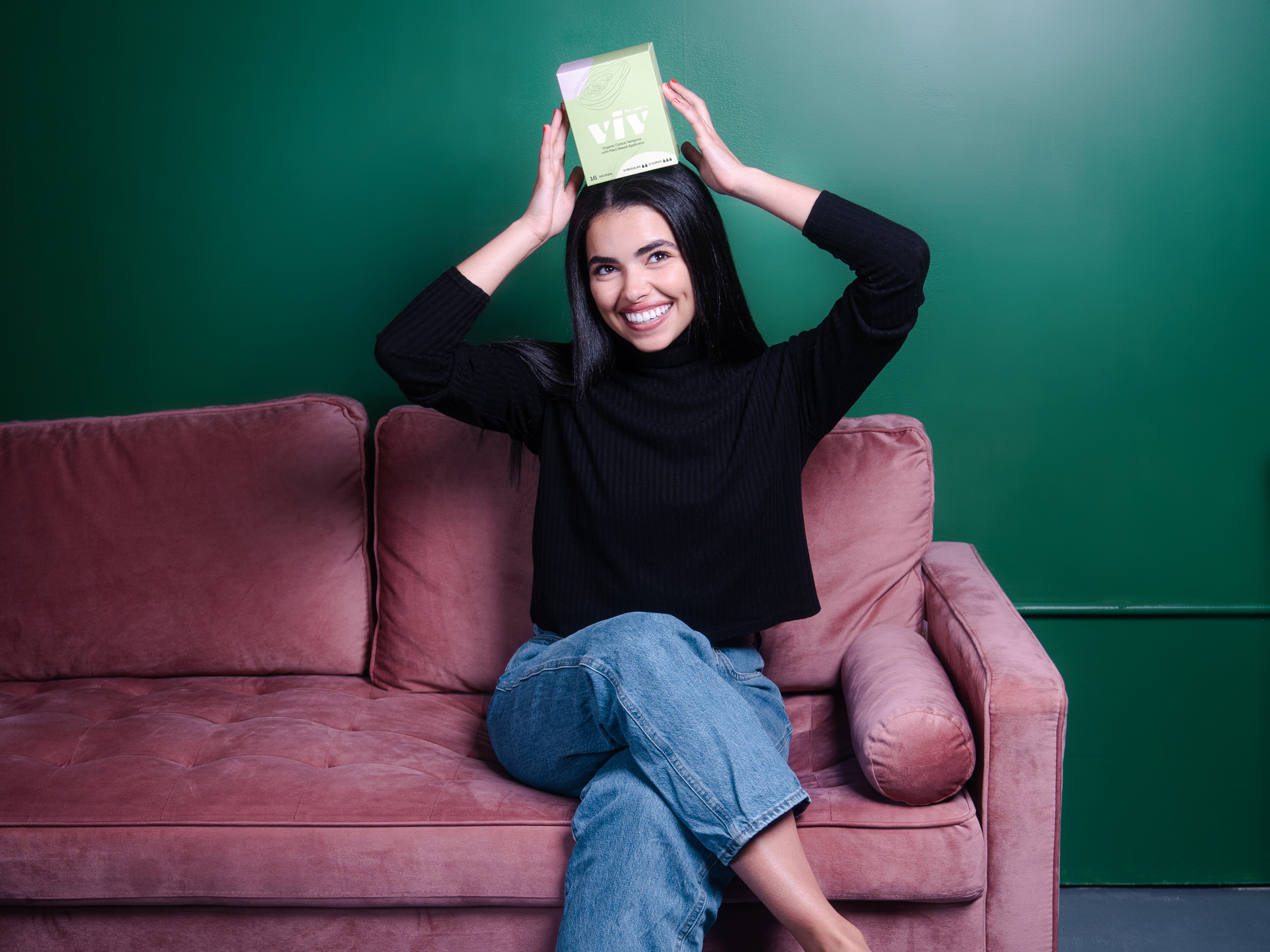 Katie Diasti, founder of Viv for your V, sitting on a couch holding a box of Viv product.