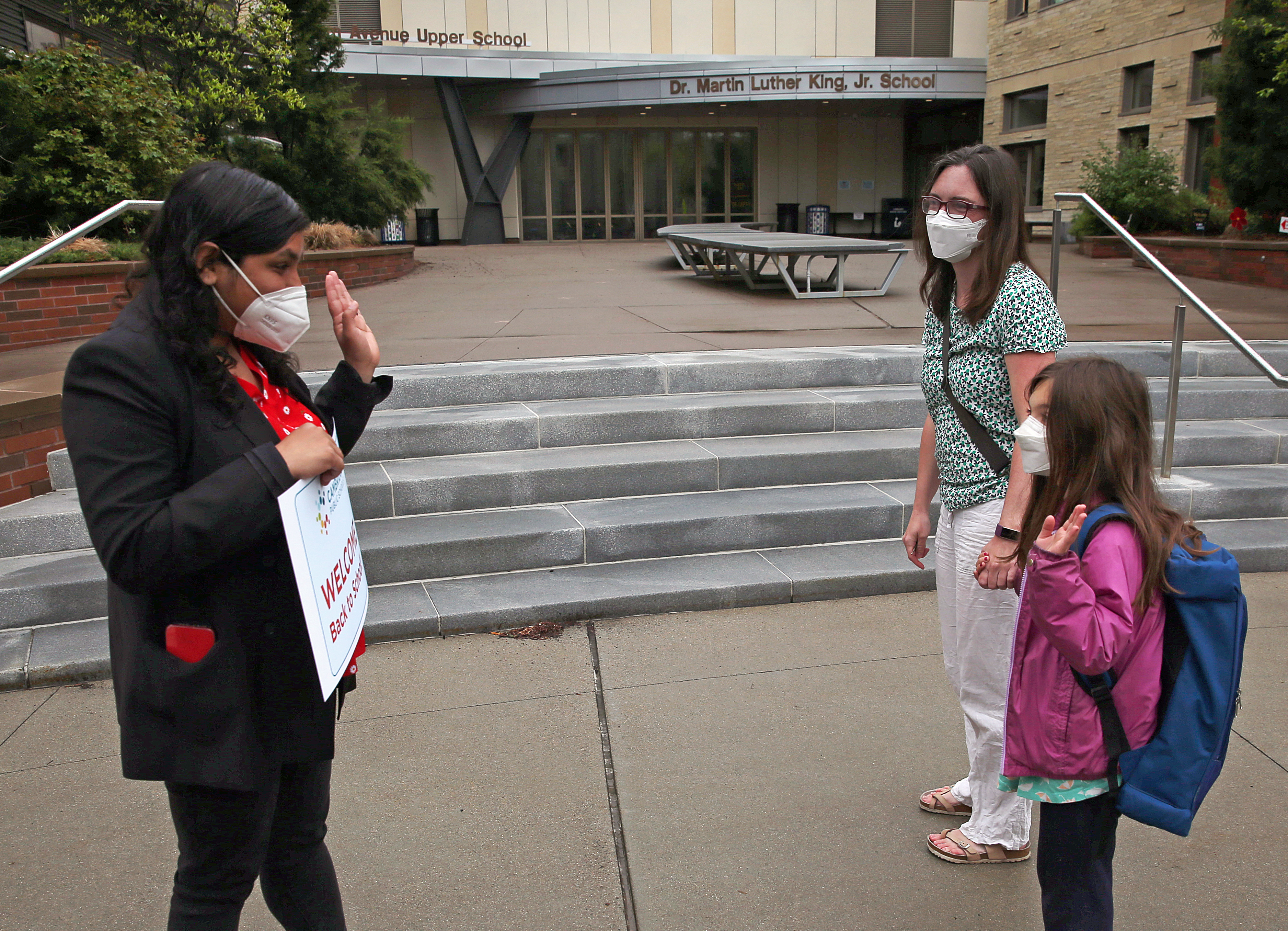 Cambridge Mayor Sumbul Siddiqui waves to Penny Hanage, a student at the Dr. Martin Luther King Jr. elementary school in Cambridge who waves back as her mother, epidemiologist Helen Jenkins, looks on.