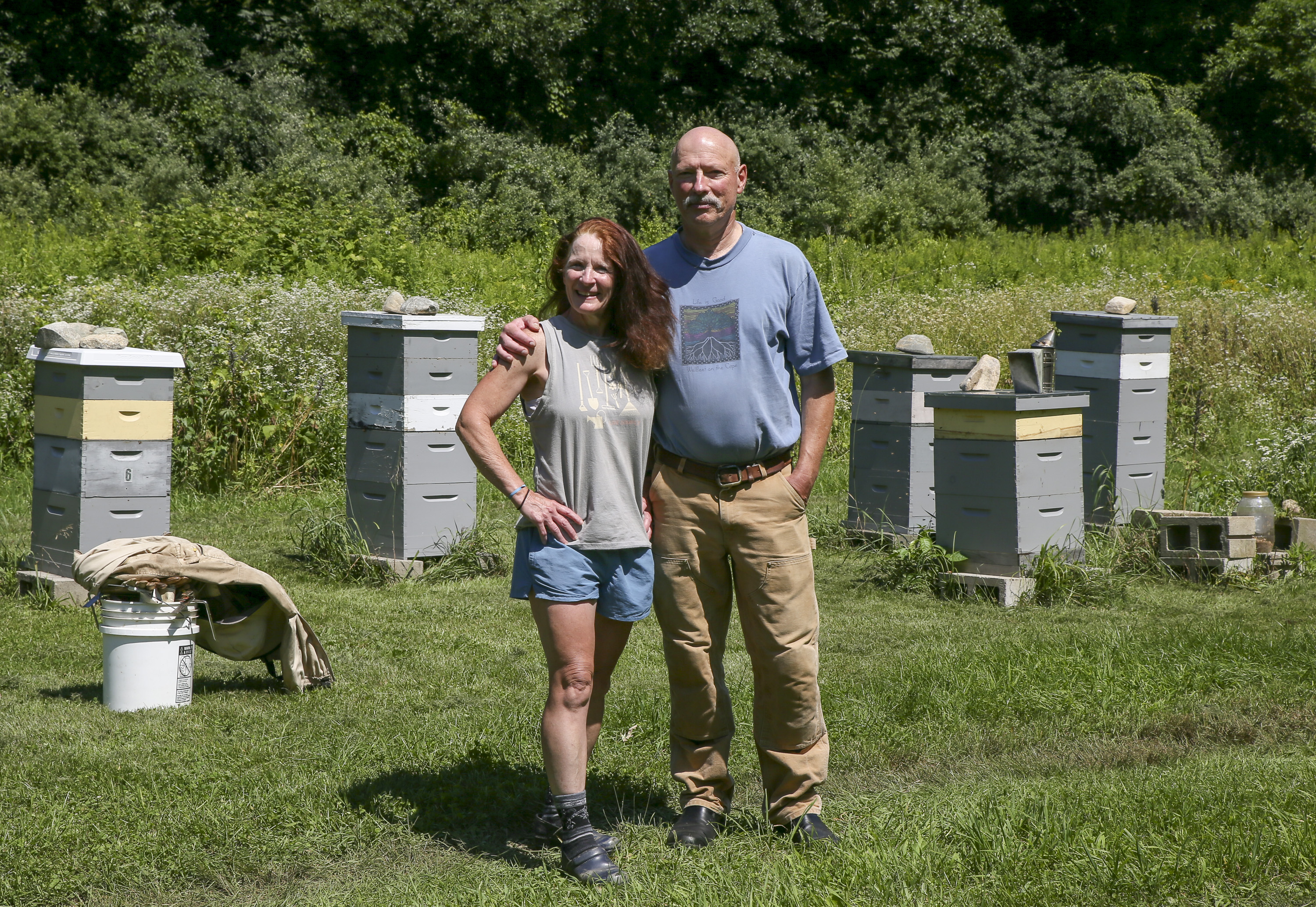 Husband and wife Geoff and Nora Neale in front of their 28 beehives, home to hundreds of thousands of bees, on their property in Topsfield.