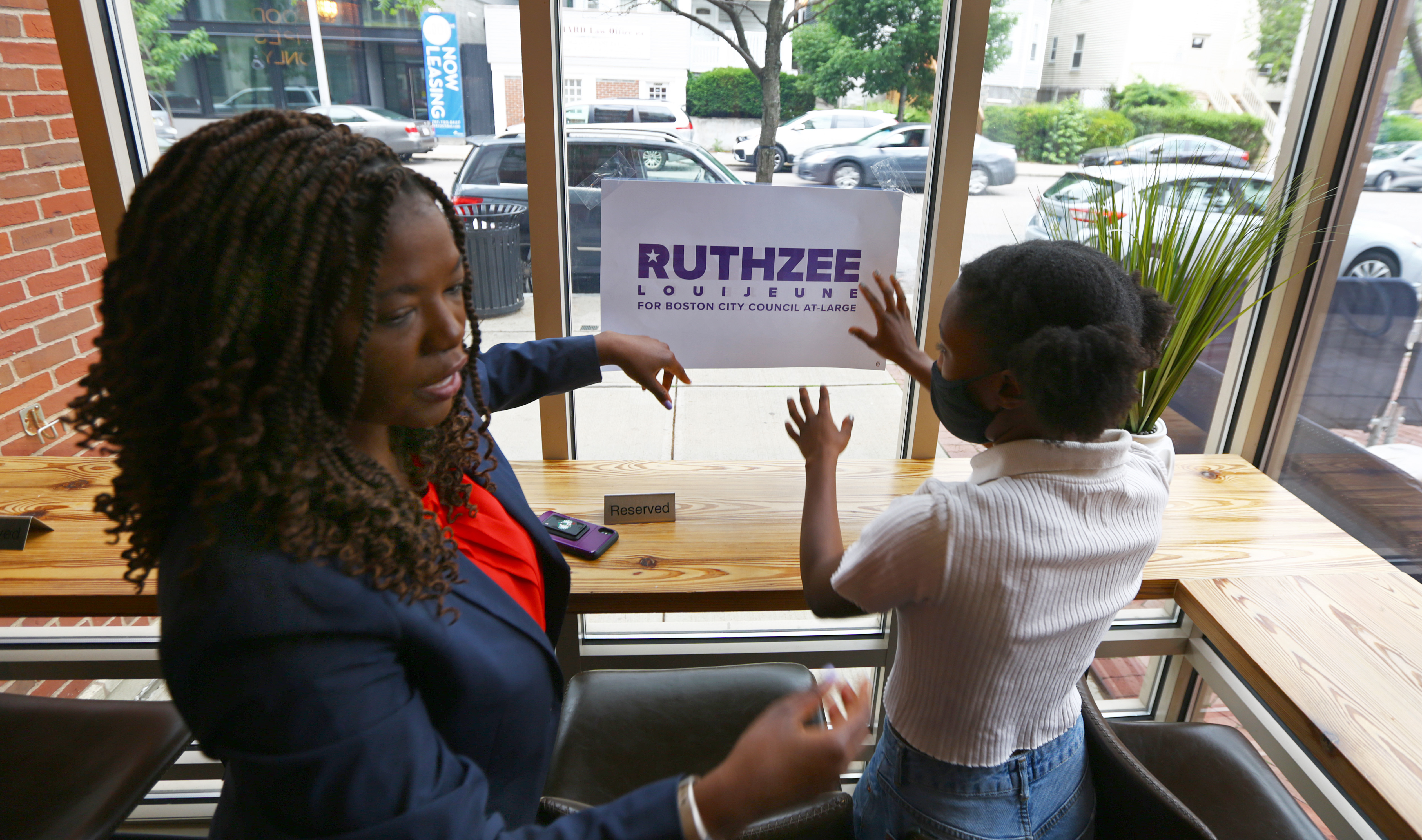 Ruthzee Louijeune, left, is a candidate for Boston City Council. She stops by Ripple Cafe and puts up one of her signs, with the help of 18-year-old campaign fellow Lillian Gibson.