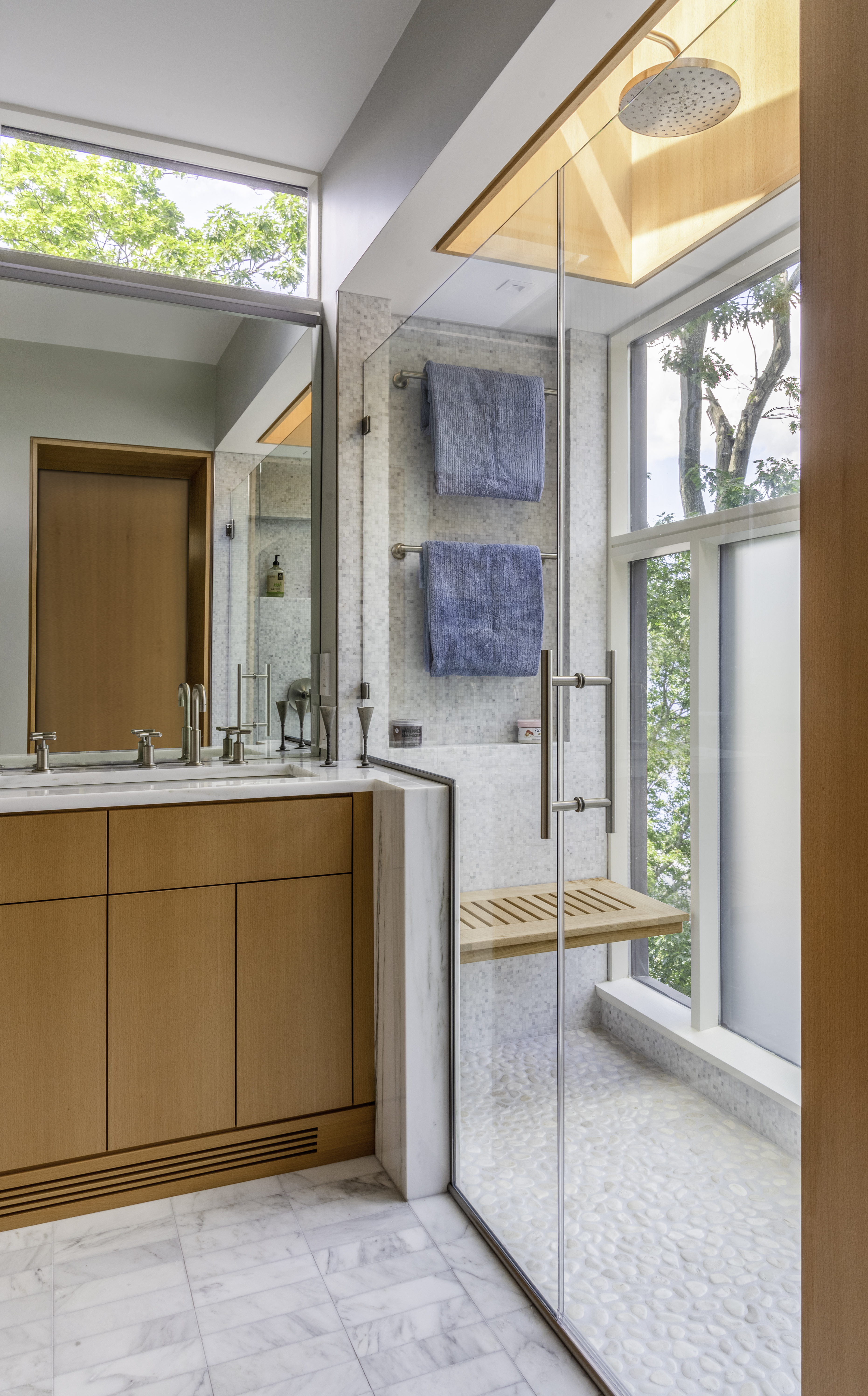 A shower with a wall of glass and an operable skylight helps bring light and air into this primary bath's shower.