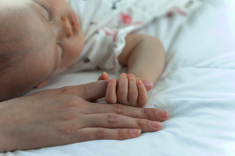 The newborn baby sleeps and grabs the mother's finger