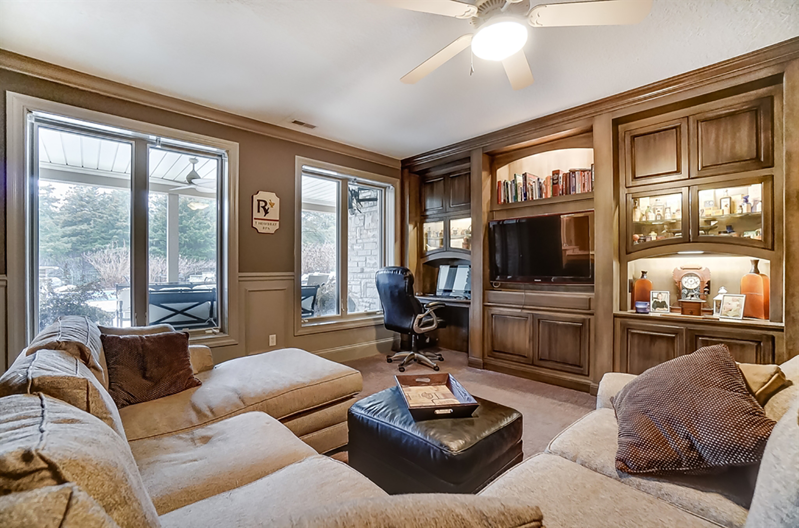 The lower-level family room has a wall of built-in storage space, glass-panel door cabinets with accent lighting, desk area and media nook. Daylight windows offer views of the outdoor kitchen. CONTRIBUTED PHOTO