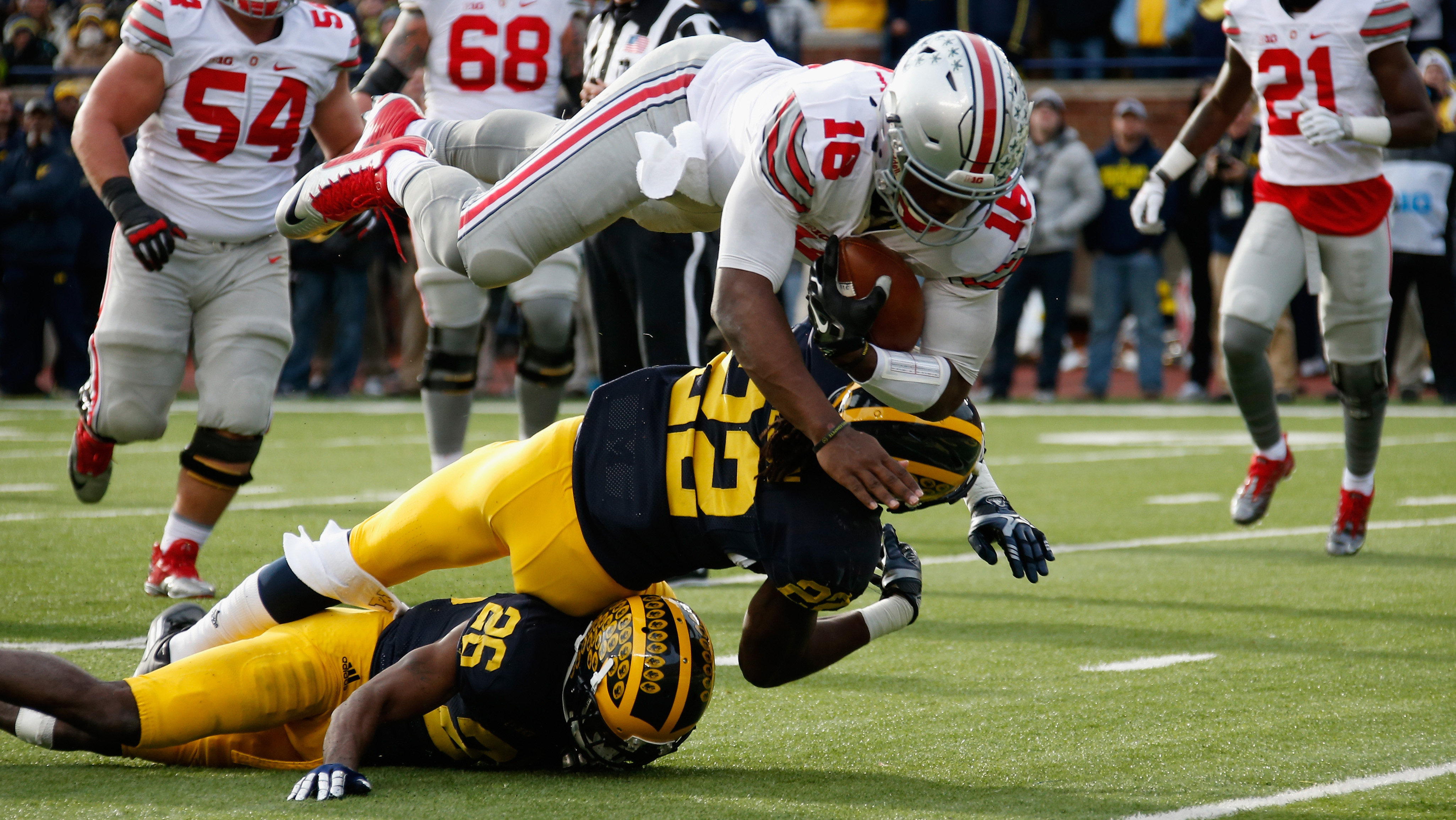 ANN ARBOR, MI - NOVEMBER 28: Quarterback J.T. Barrett #16 of the Ohio State Buckeyes dives over Jarrod Wilson #22 and Jourdan Lewis #26 of the Michigan Wolverines for a third quarter touchdown at Michigan Stadium on November 28, 2015 in Ann Arbor, Michigan. (Photo by Gregory Shamus/Getty Images)