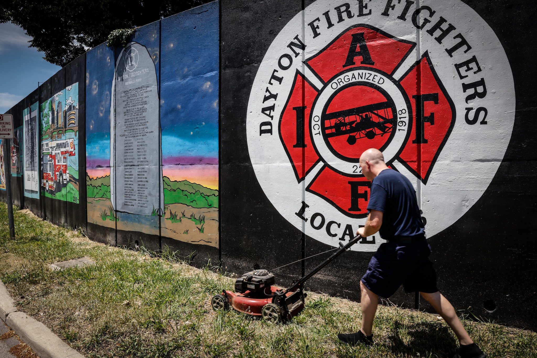 Dayton Firefighter Mike Brown cuts grass in front of a a mural depicting the history of Dayton firefighting on Buckeye St. Friday June 24, 2022. On Saturday at 1:00p.m. there will be a dedication of the mural and the public is invited. JIM NOELKER/STAFF