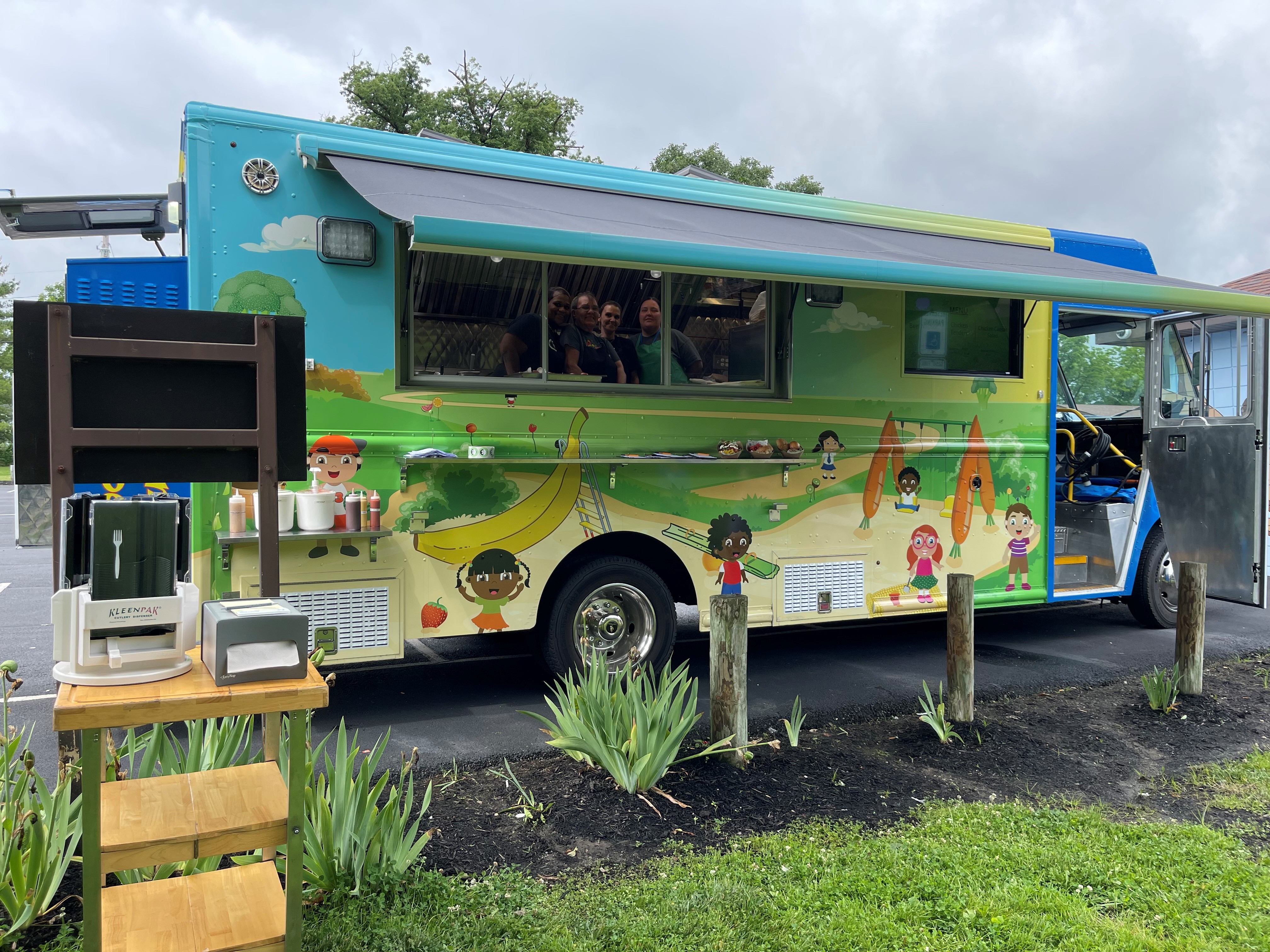 Staff who work in Hamilton City Schools cafeterias are seen working at the Big Blue Food Truck in Crawford Woods.  The truck goes around town offering free lunches to students during the summer.  Adults can purchase a meal for $4.  MANDY GAMBRELL/STAFF