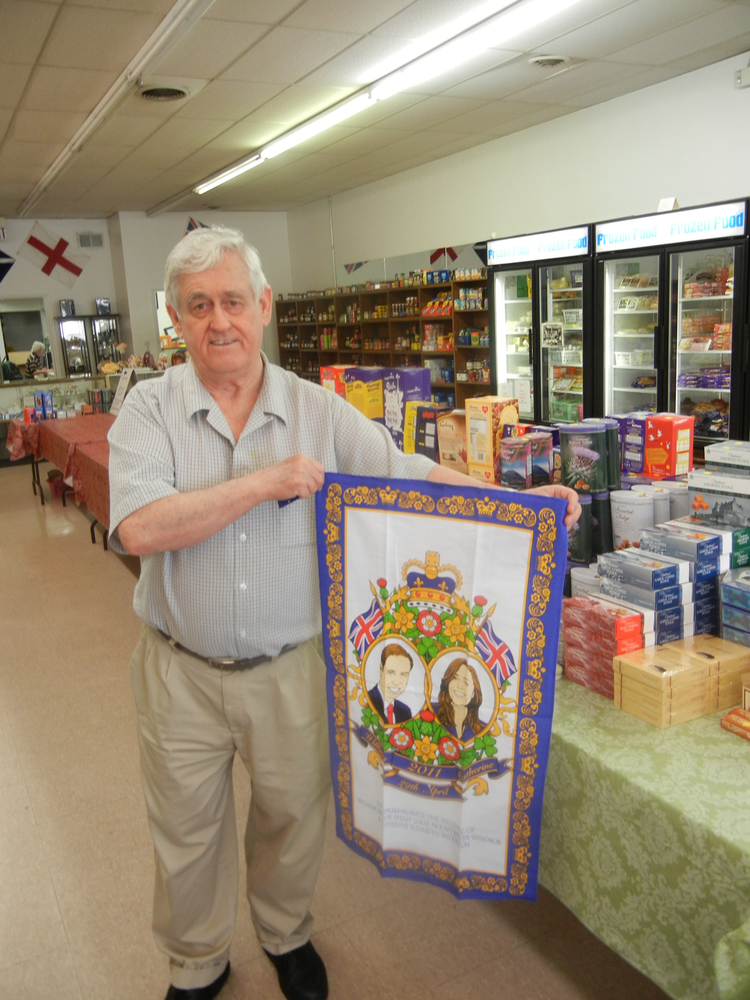 Harry Caswell, owner of Wise Choice British Foods, Gifts and Candies in Huber Heights, holds of a wall hanging featuring a image of Prince William and Kate Middleton. staff photo by Amelia Robinson