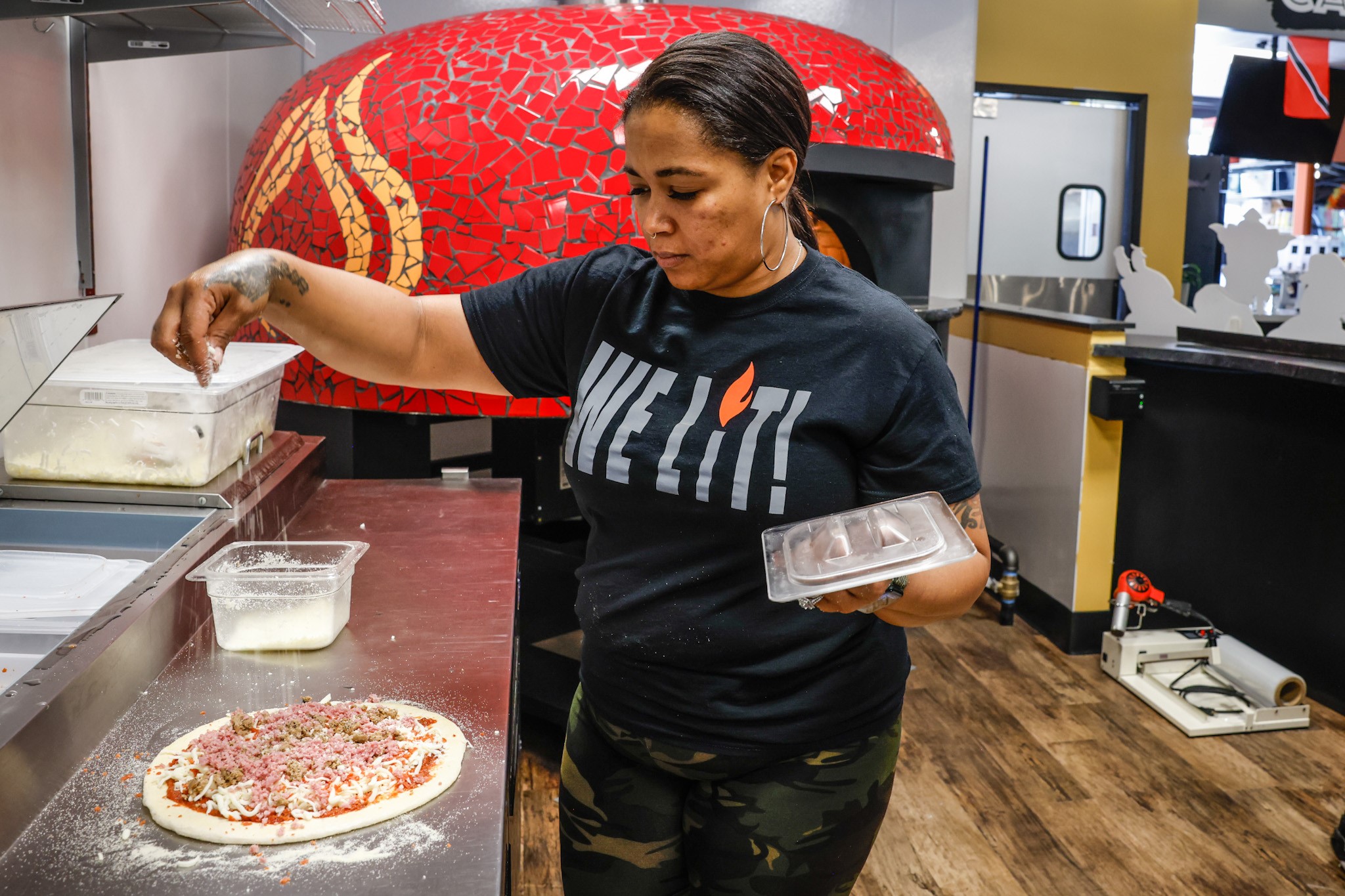 ILLY'S Fire Pizza owner, Kelly Gunn sprinkles toppings on a pizza before sliding it into the oven. ILLY'S Fire Pizza is located inside West Social Tap and Table, located at 1100 West Third St. in Dayton. JIM NOELKER/STAFF