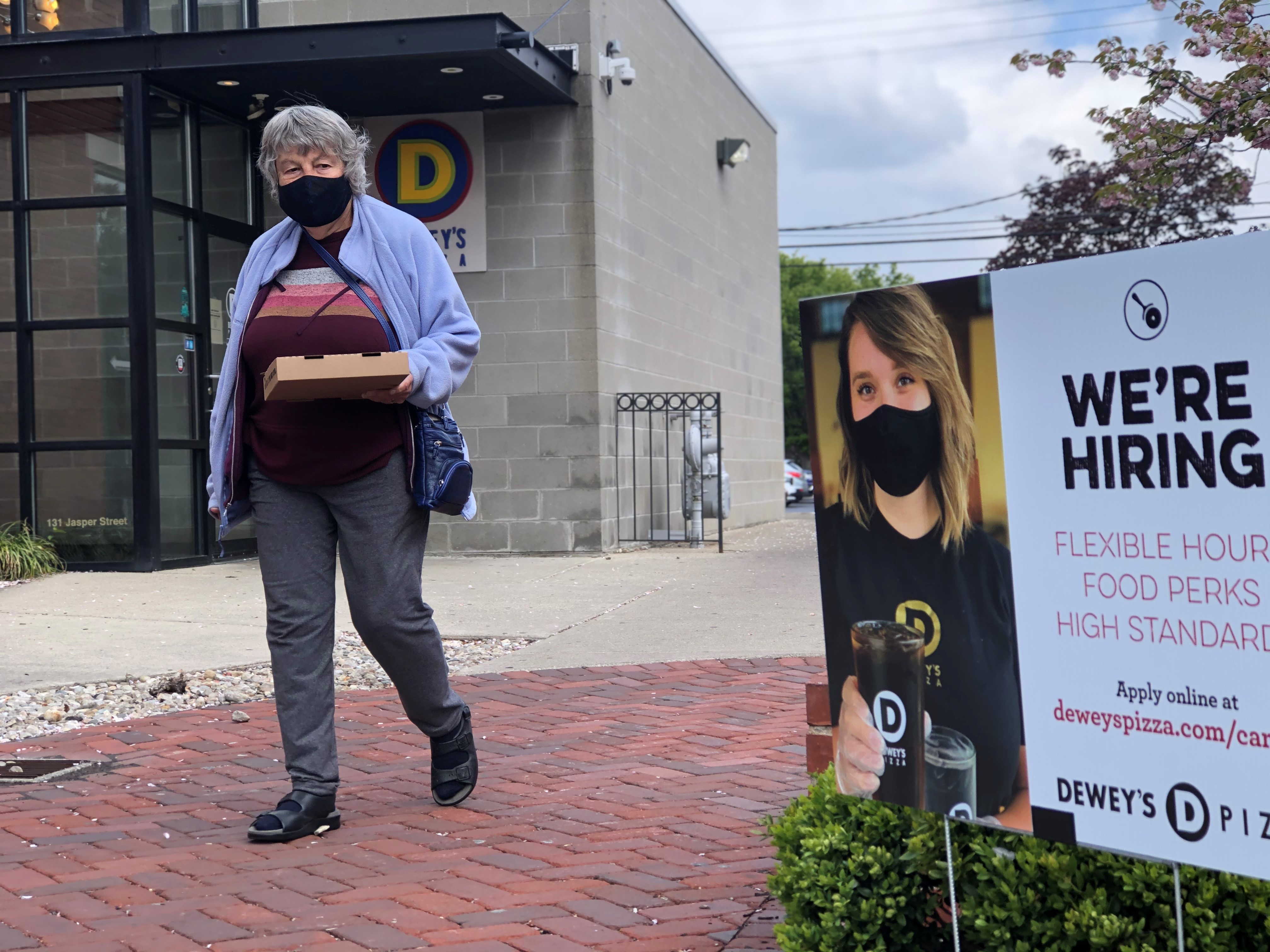A customer of Dewey's Pizza in Dayton walks by a "We're Hiring" sign. CORNELIUS FROLIK / STAFF