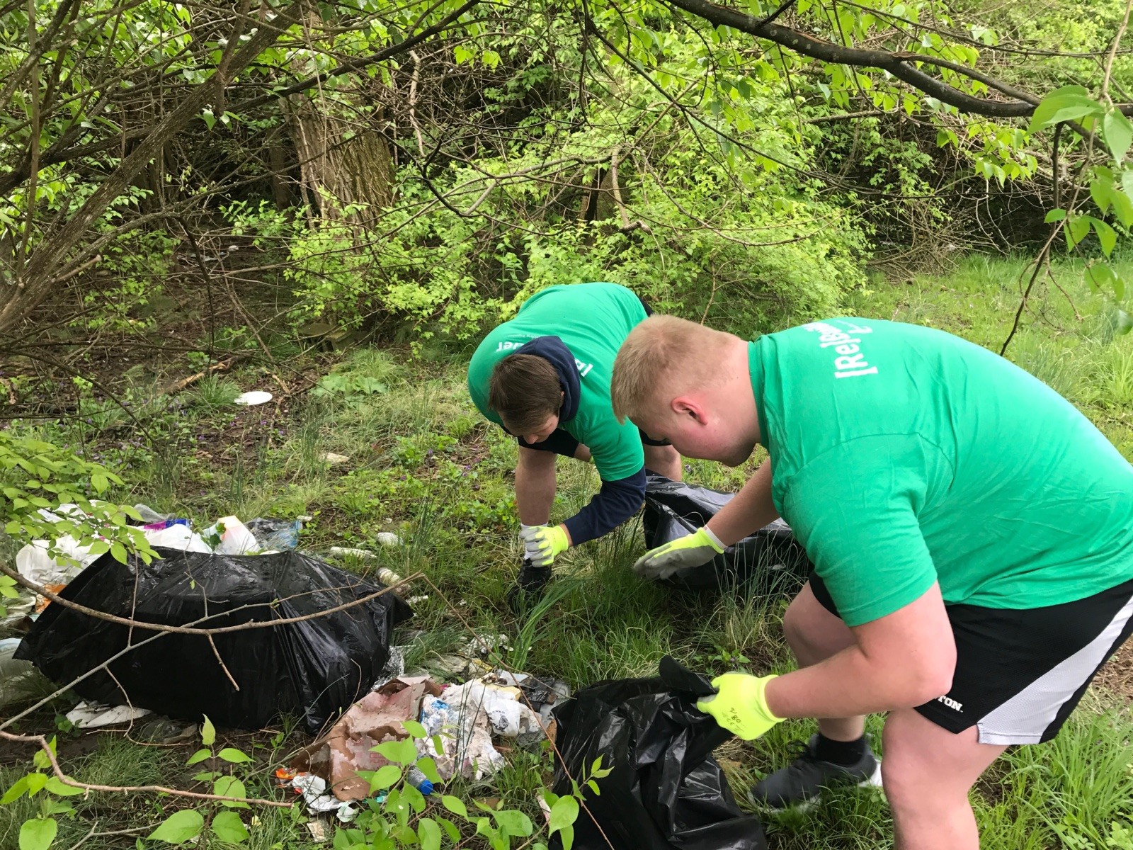 Dayton Flyers defensive tackle Joe Gits (right) and center Dylan DeMaison pick up trash while trying to avoid the numerous discarded drug needles they found as they cleaned up around an abandoned house of Weaver Street Saturday. (Tom Archdeacon photo)