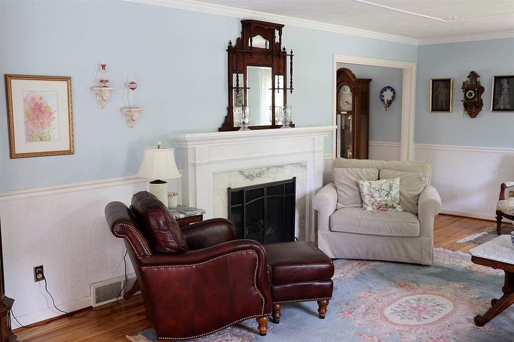 The formal living room has plaster details, including a ceiling medallion and roping. A fireplace has marble surround that matches the foyer flooring and an ornate wood mantel. Windows fill the room with natural light. Contributed photo