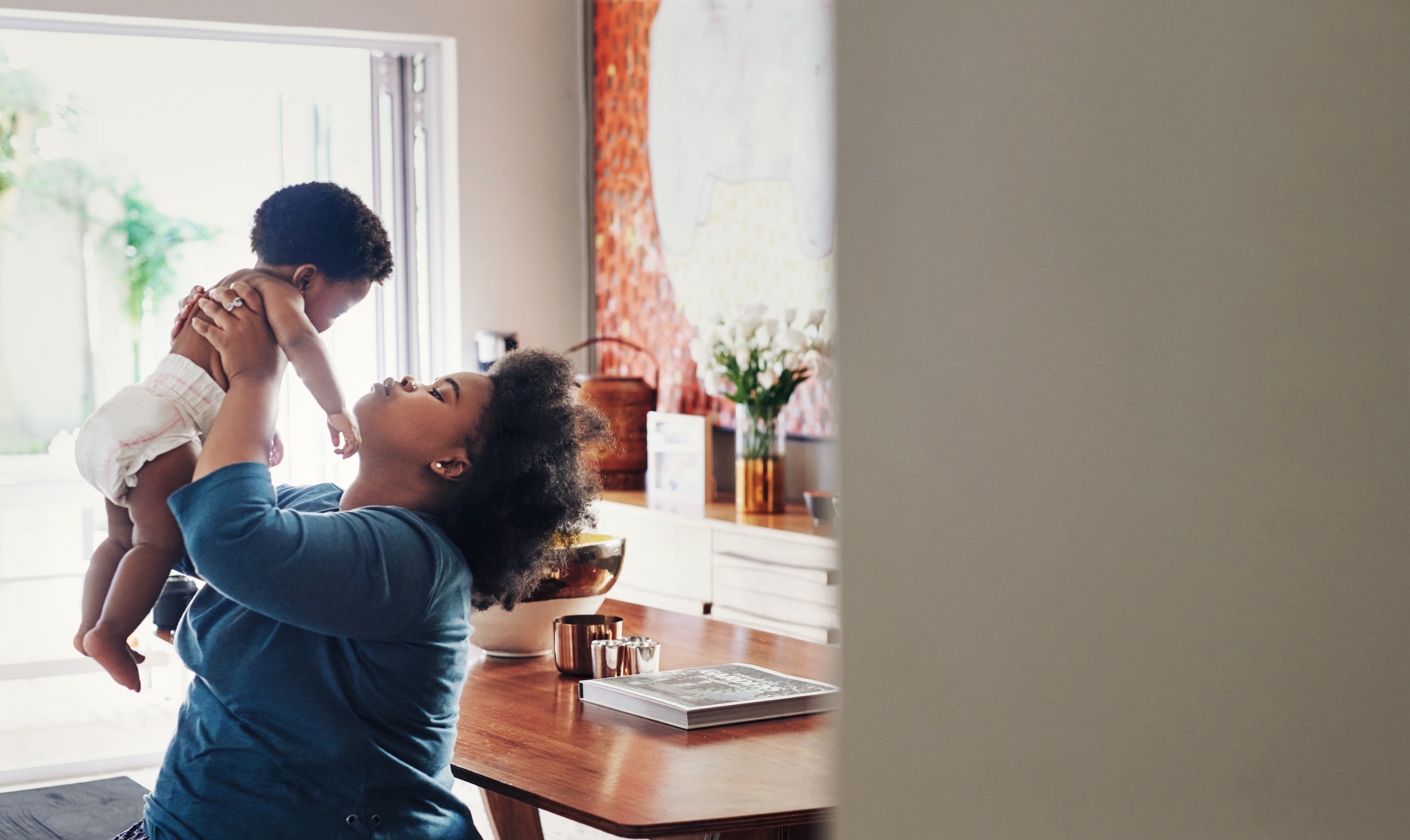 An African-American mother holds her infant in the air lovingly.