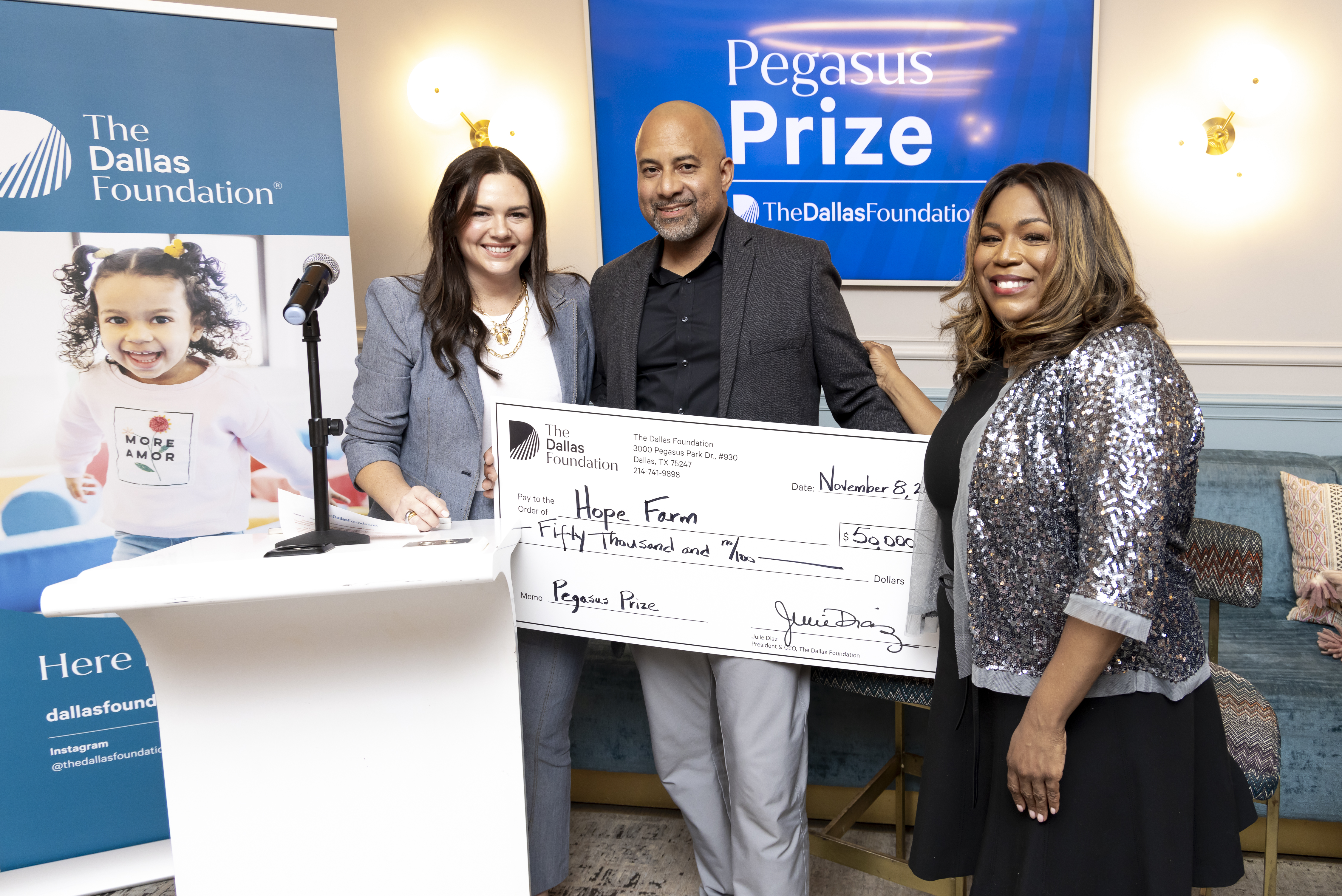 Two well-dressed women stand on opposite sides of a man holding an oversized check for...