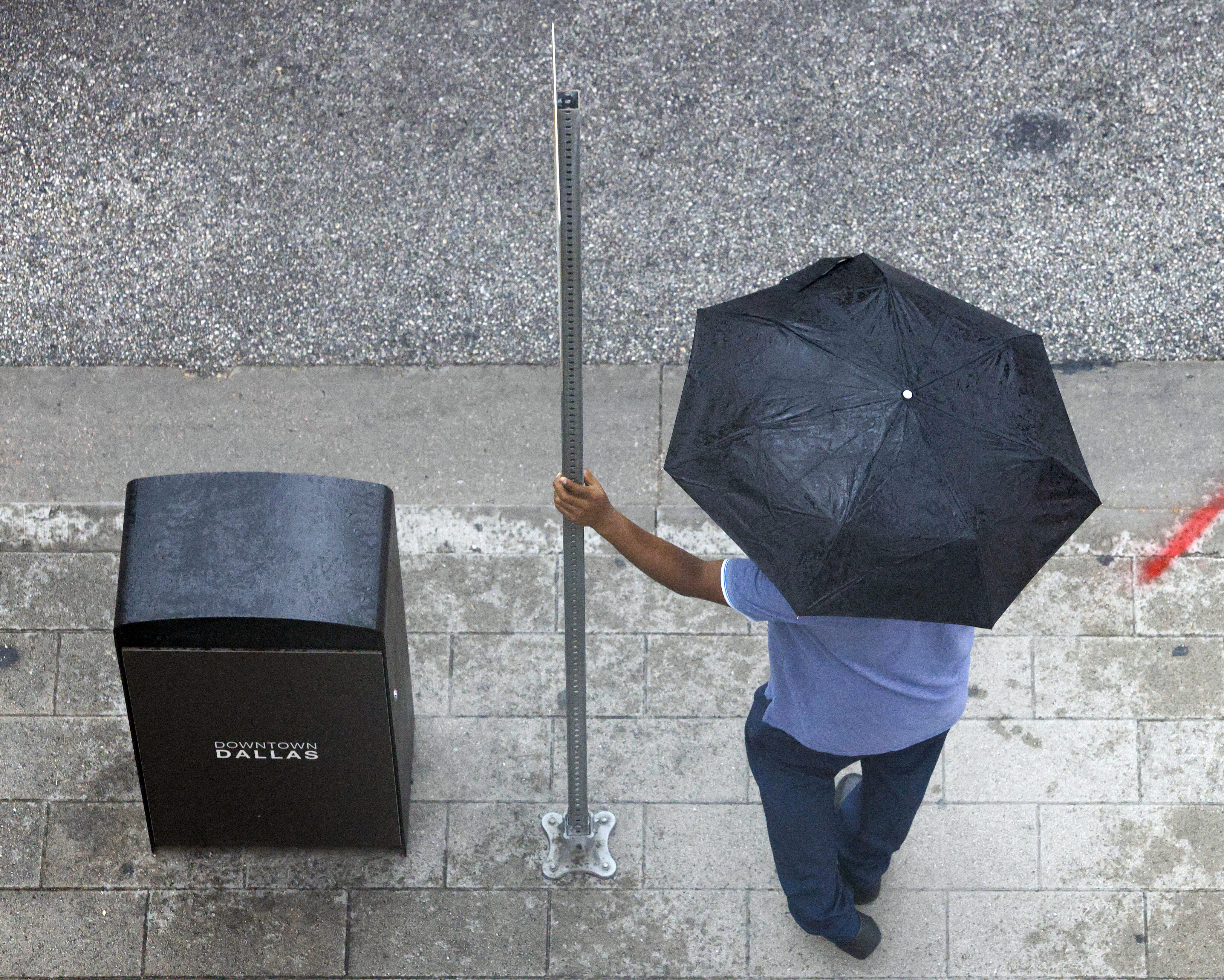 A man waits for a DART bus under an umbrella as rain falls in downtown Dallas, Wednesday,...
