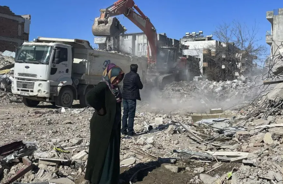 Los padres de Taha Erdem, la madre Zeliha Erdem, a la izquierda, y el padre Ali Erdem, junto a los escombros del edificio donde Tahan quedó atrapado tras el terremoto del 6 de febrero, en Adiyaman, Turquía. (AP Photo/Mehmet Mucahit Ceylan)