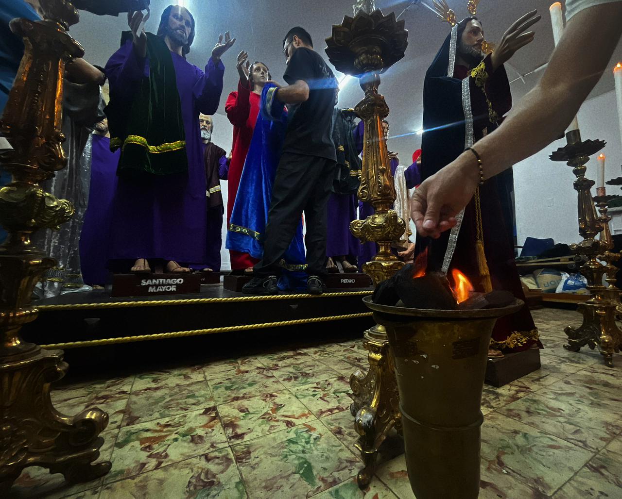 Integrante de la Cofradía Pasionista prende el incienso mientras otro organiza las figuras de los apóstoles durante los ensayos nocturnos previos a las procesiones.