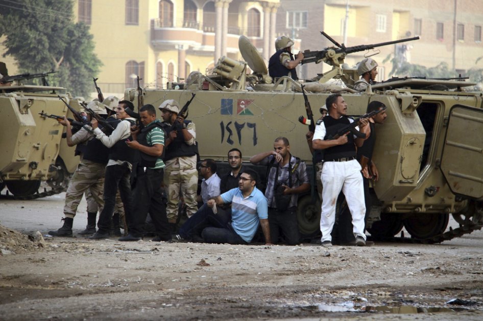 Soldados egipcios y periodistas locales se cubren tras un vehículo armado durante una operación contra un grupo de hombres armados en un suburbio de El Cairo, Egipto./ EFE