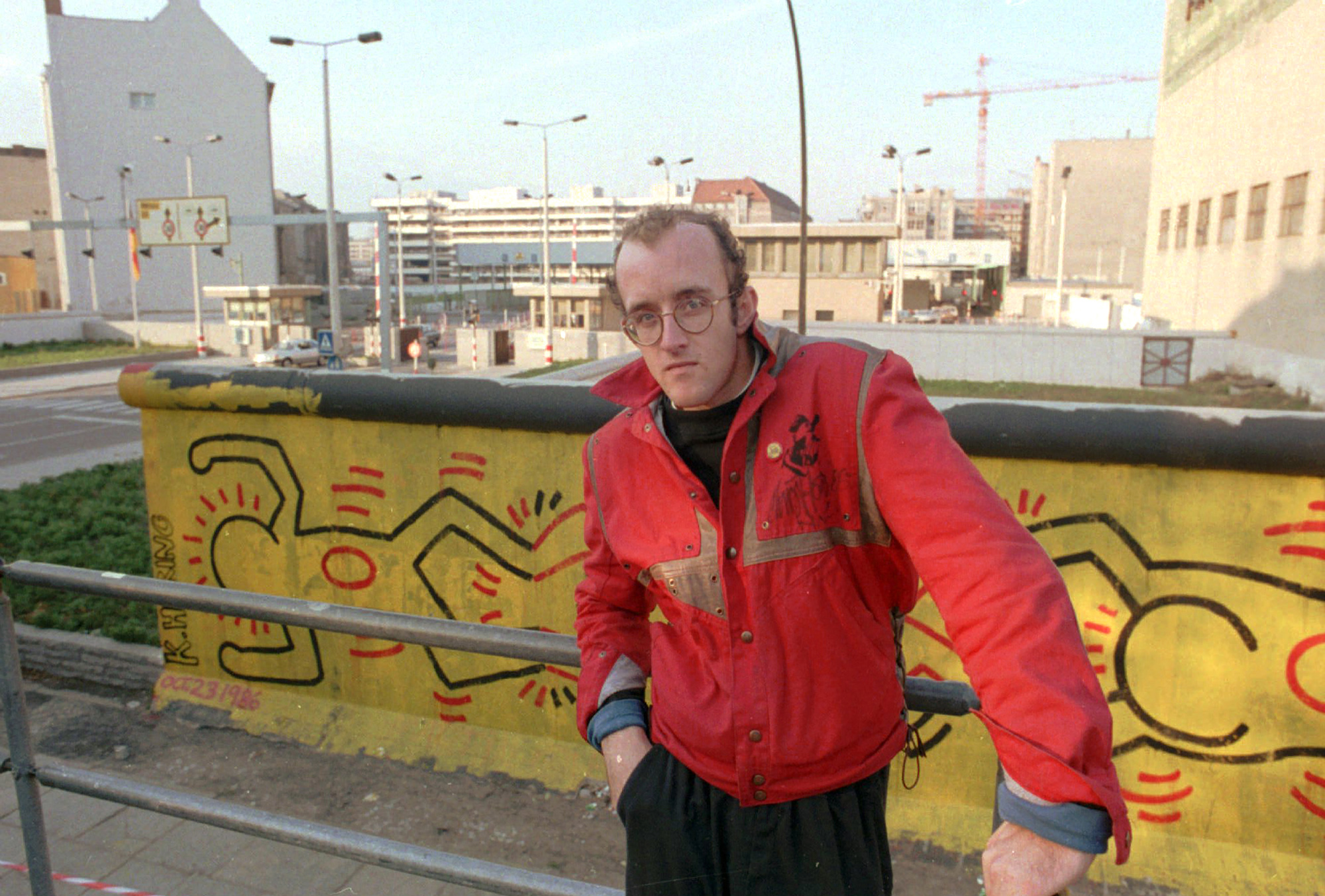 FILE - In this October 1986 file photo, artist Keith Haring stands in front of part of the Berlin Wall that he painted with a crawling baby in Berlin. The Berlin Wall came down in late 1989. Haring died of AIDS Feb. 16, 1990, at age 31.(AP Photo/Elke Bruhn-Hoffmann, File)
