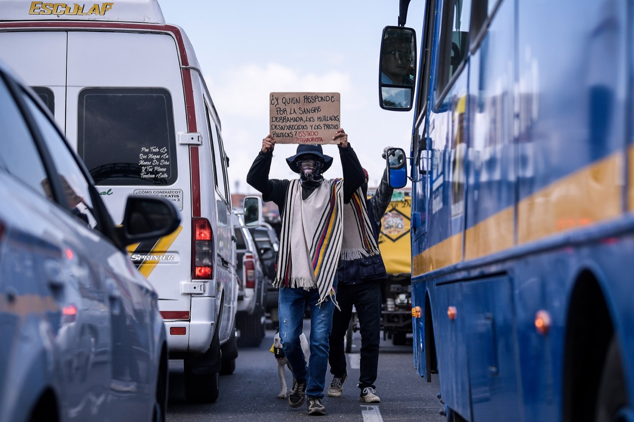 Manifestantes caminando entre el tráfico del sur de la ciudad con carteles de protesta.