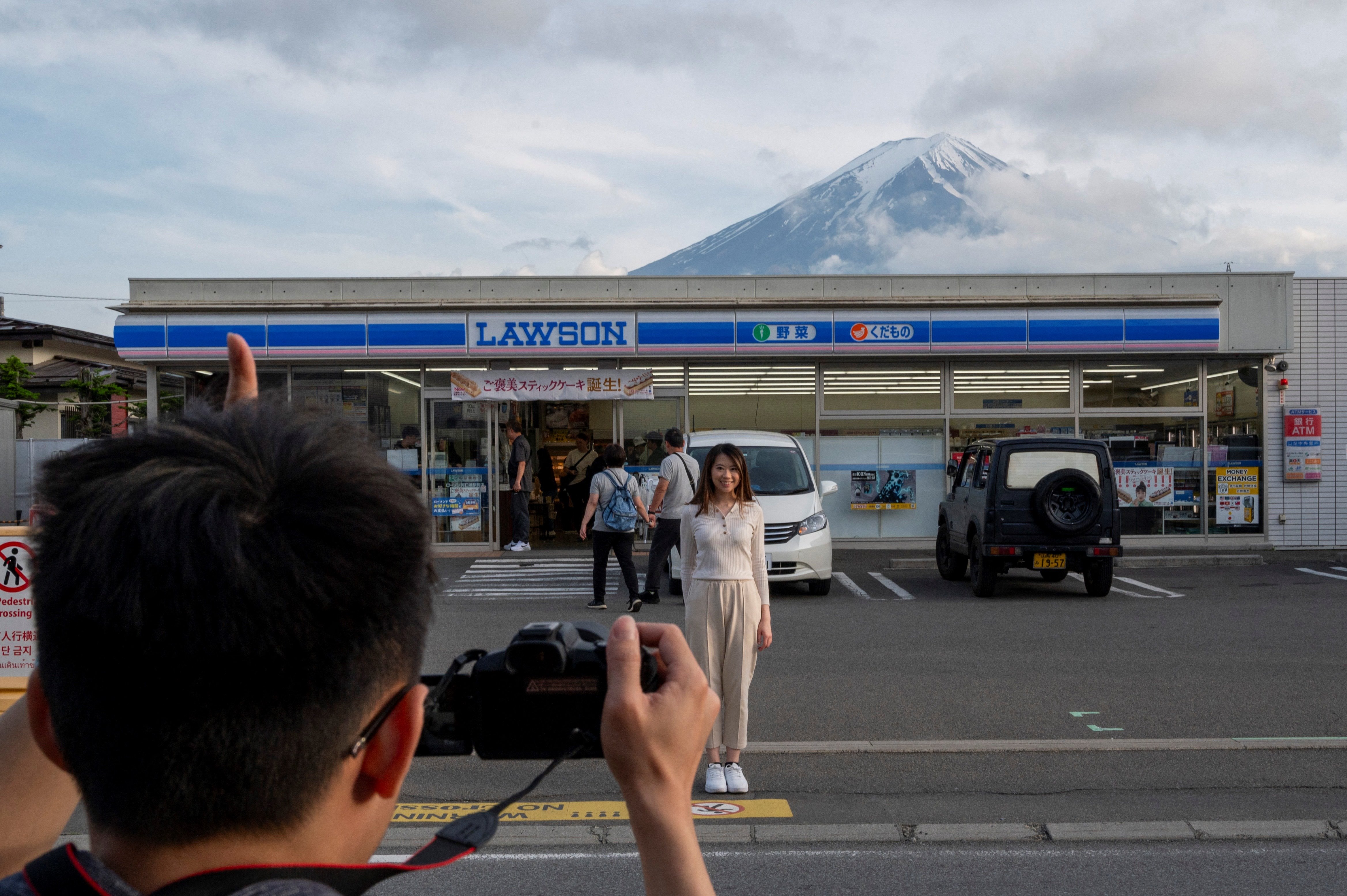 TOPSHOT - This photo taken on May 20, 2024 shows tourists taking pictures of Mount Fuji from opposite a convenience store in the town of Fujikawaguchiko, Yamanashi prefecture.