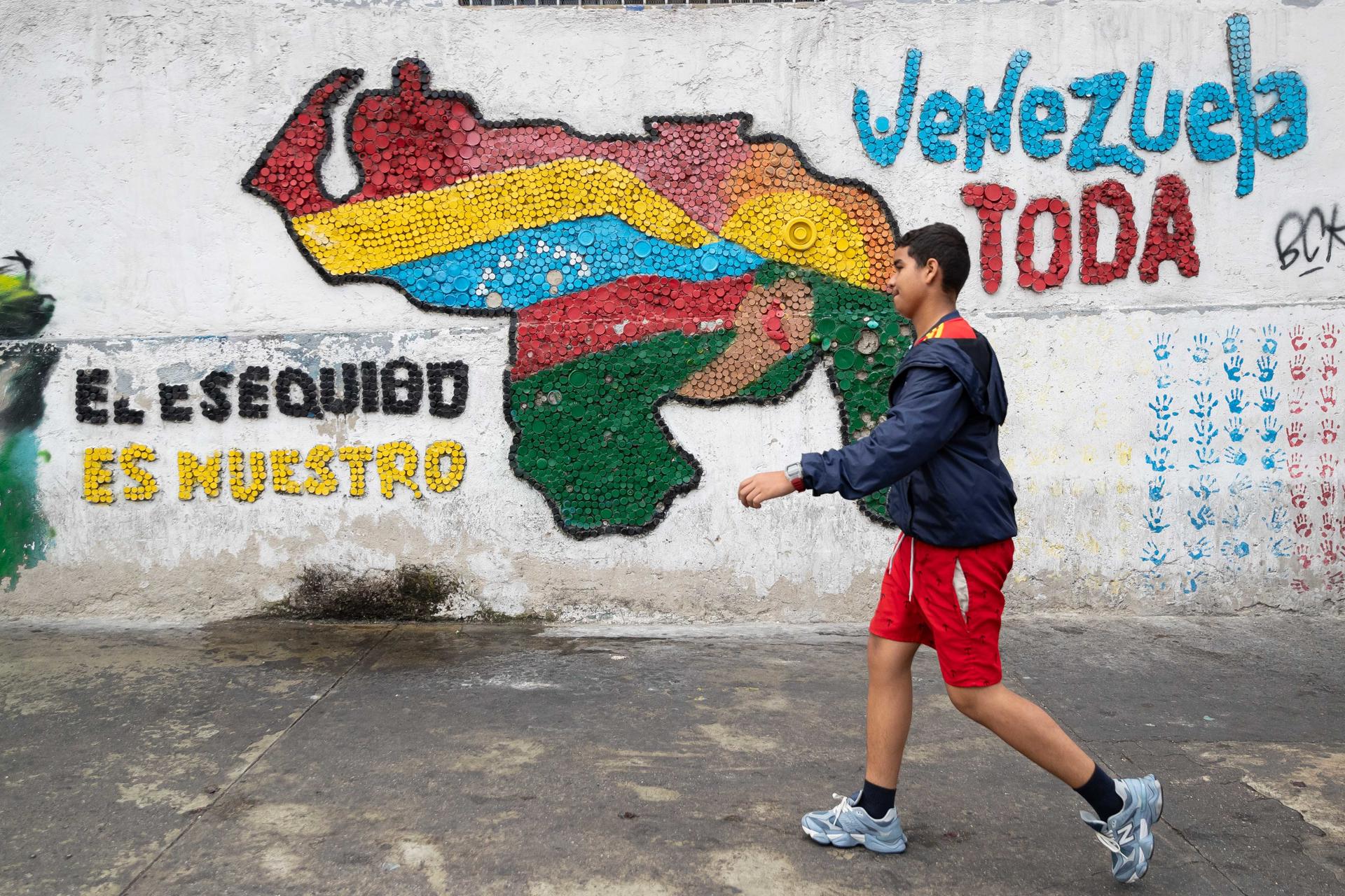 AME9332. CARACAS (VENEZUELA), 21/04/2025.- Fotografía del 2 de abril del 2025 de una persona caminando frente a un mural con el mapa de Venezuela en Caracas (Venezuela). El descubrimiento de yacimientos petrolíferos en altamar por parte de Guyana, que con la reciente llegada del buque 'One Guyana' espera elevar su capacidad de producción diaria a unos 900.000 barriles de crudo, ha añadido una dimensión política y económica a la disputa territorial de hace más de un siglo entre este país y Venezuela por la soberanía del Esequibo, dijeron expertos a EFE. EFE/ Ronald Peña
