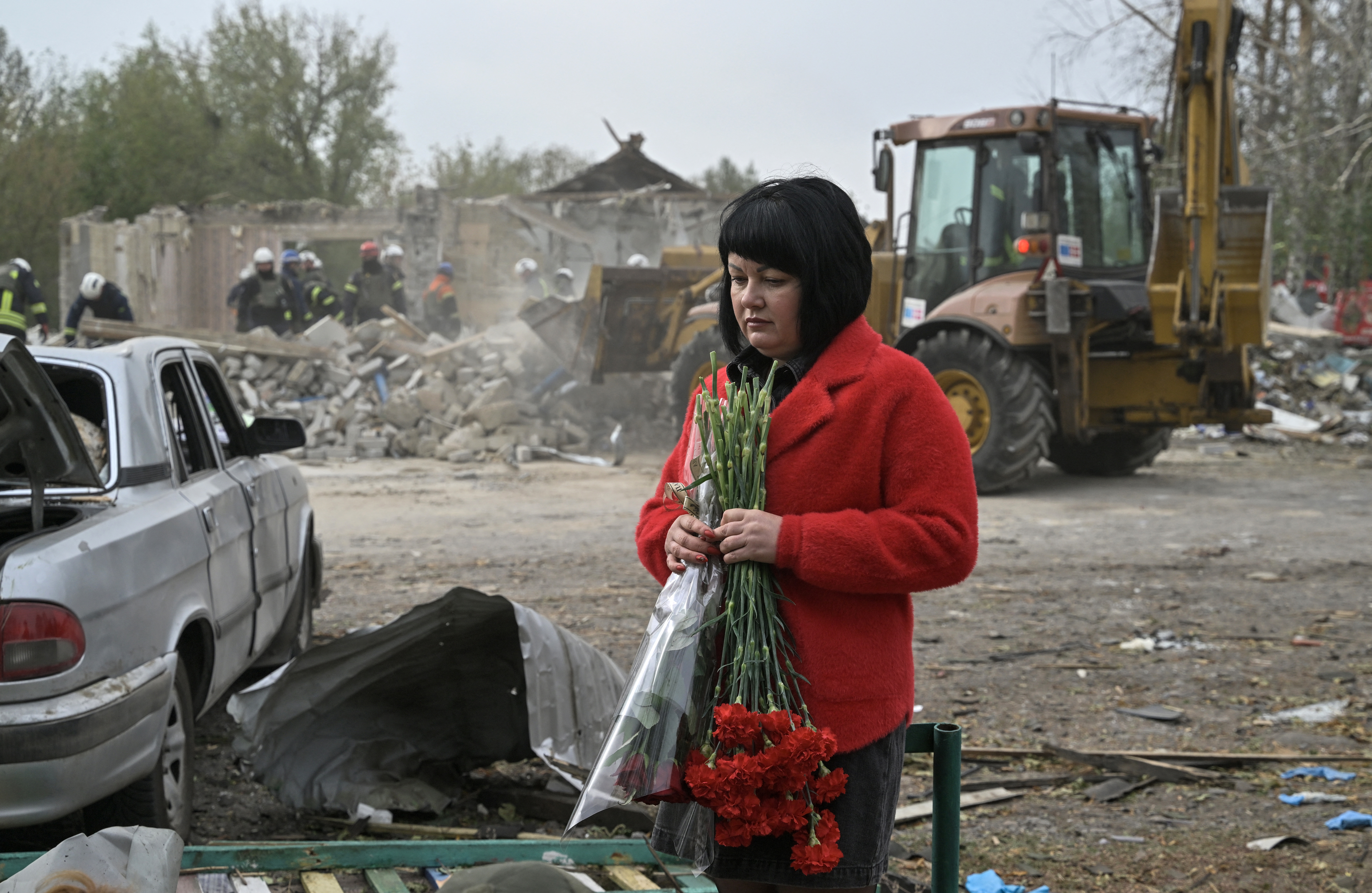 Una mujer sostiene un ramo de flores en sus manos, mientras los rescatistas ucranianos trabajan para retirar los escombros que dejó el ataque ruso en Groza.
