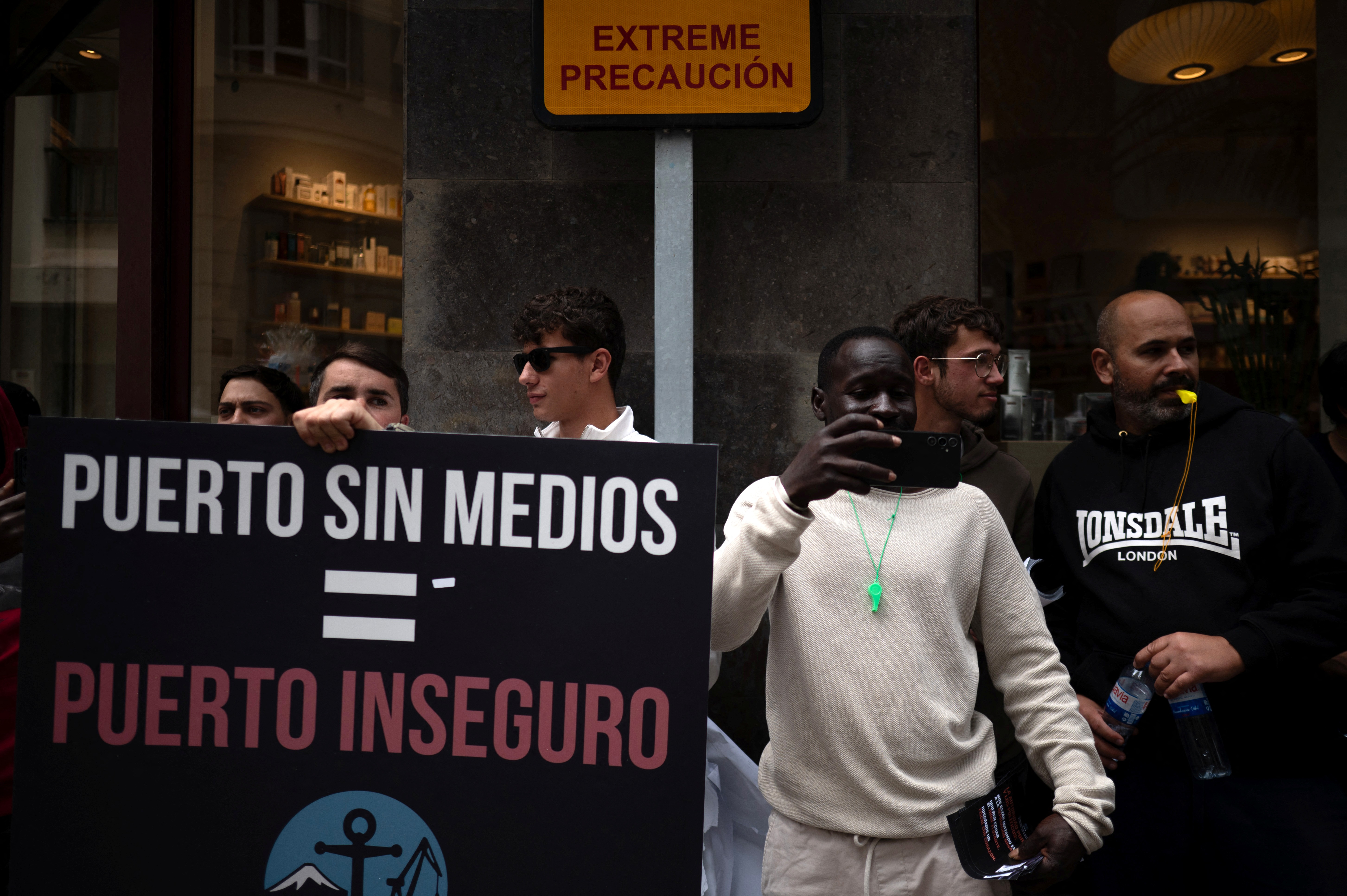 Dockers hold a banner reading 'Workers of Tenerife Port - TPT (Trabajadores del Puerto de Tenerife) - Port without means, Port unsafe' as they protest against the arrival of a cruise ship affected by hantavirus in Santa Cruz de Tenerife on May 8, 2026. Passengers aboard the MV Hondius cruise ship affected by a deadly hantavirus outbreak will start being flown to their countries of origin after the vessel arrives on the Canary island of Tenerife on May 10, 2026, the Spanish government said. (Photo by JORGE GUERRERO / AFP)