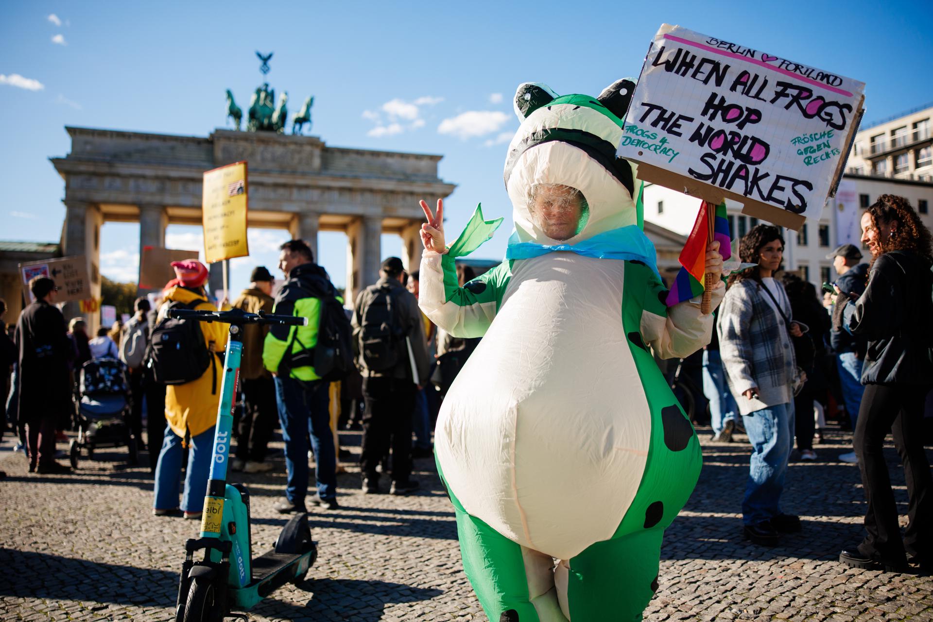 Una persona vestida con un disfraz de rana sostiene un cartel que dice “Cuando todas las ranas saltan, el mundo tiembla” durante una manifestación frente a la Puerta de Brandeburgo en Berlín, Alemania.
