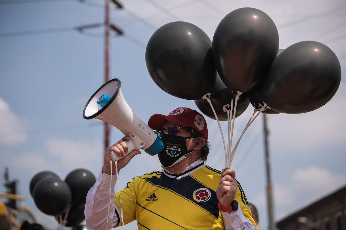 Un hombre con un megáfono y cuatro globos en la otra mano.