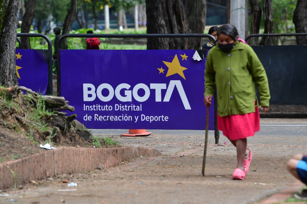 Una señora con bastón camina enfrente a vallas del Instituto de Recreación de deporte. La Alcaldía ha expresado que la solución para los indígenas la debe dar el gobierno nacional.