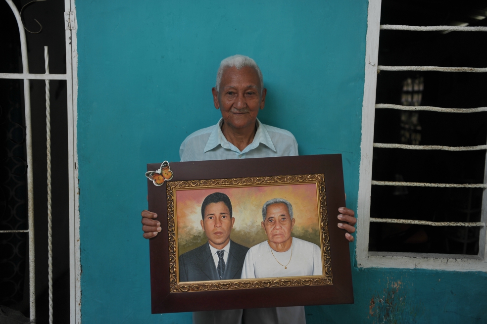 Diego García, de 87 años, reclamante de los predios de Diana María, en la vereda Macondo del municipio de Zona Bananera en el Magdalena, sostiene el cuadro de su hijo y su esposa, el primero asesinado por paramilitares el 12 de septiembre de 2001, en la finca que hoy, pese a su edad avanzada, sigue luchando junto a otras 46 familias. / Gustavo Torrijos - El Espectador.
