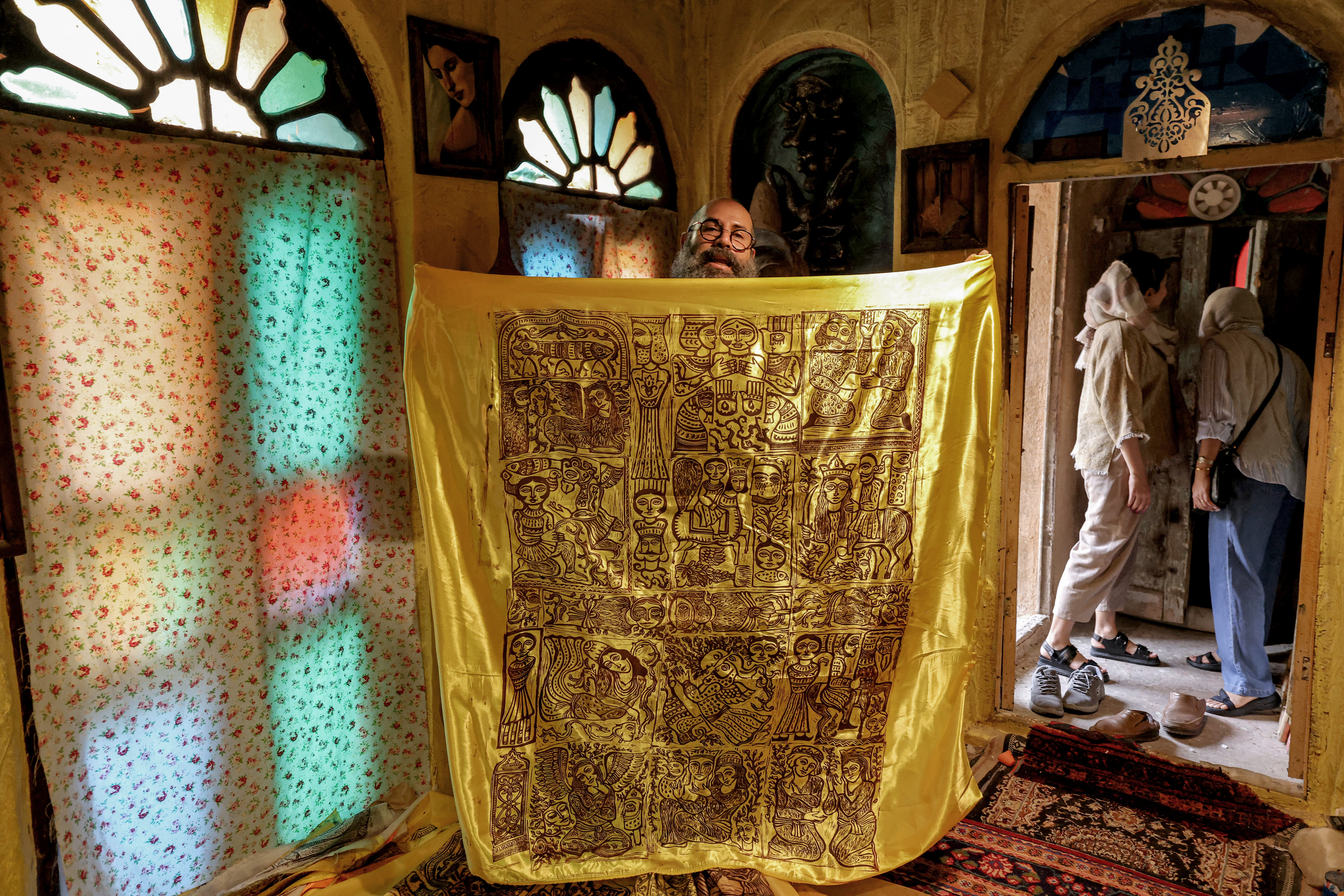 (FILES) Adel Yazdi, an Iranian artist who has transformed an alley in one of the old neighbourhoods of Shiraz into an open air permanent art gallery, shows one of his printed scarves as women visit his workshop in the central Iranian city on May 14, 2024.